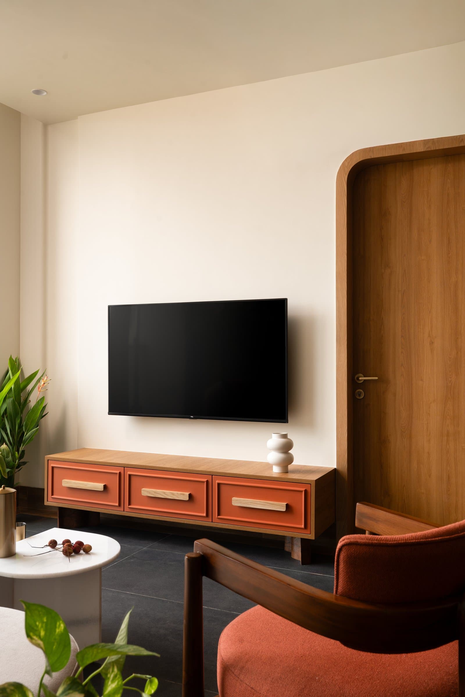 The media wall, where a warm timber console with terracotta panels sits beneath a tall arched door