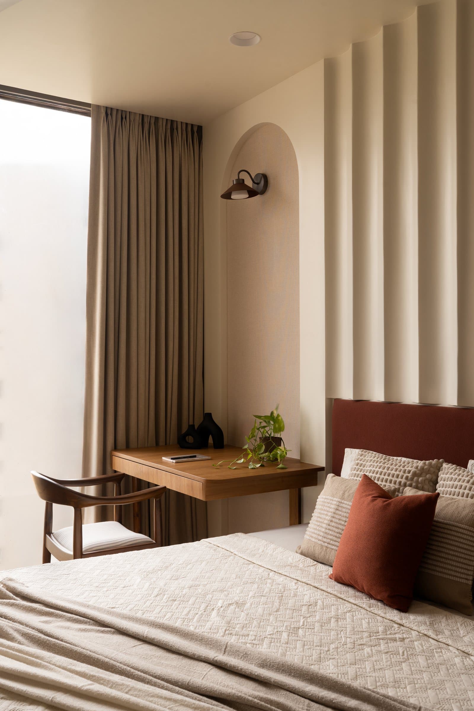 The primary bedroom, where fluted panelling and a rust-toned headboard anchor a quiet work alcove