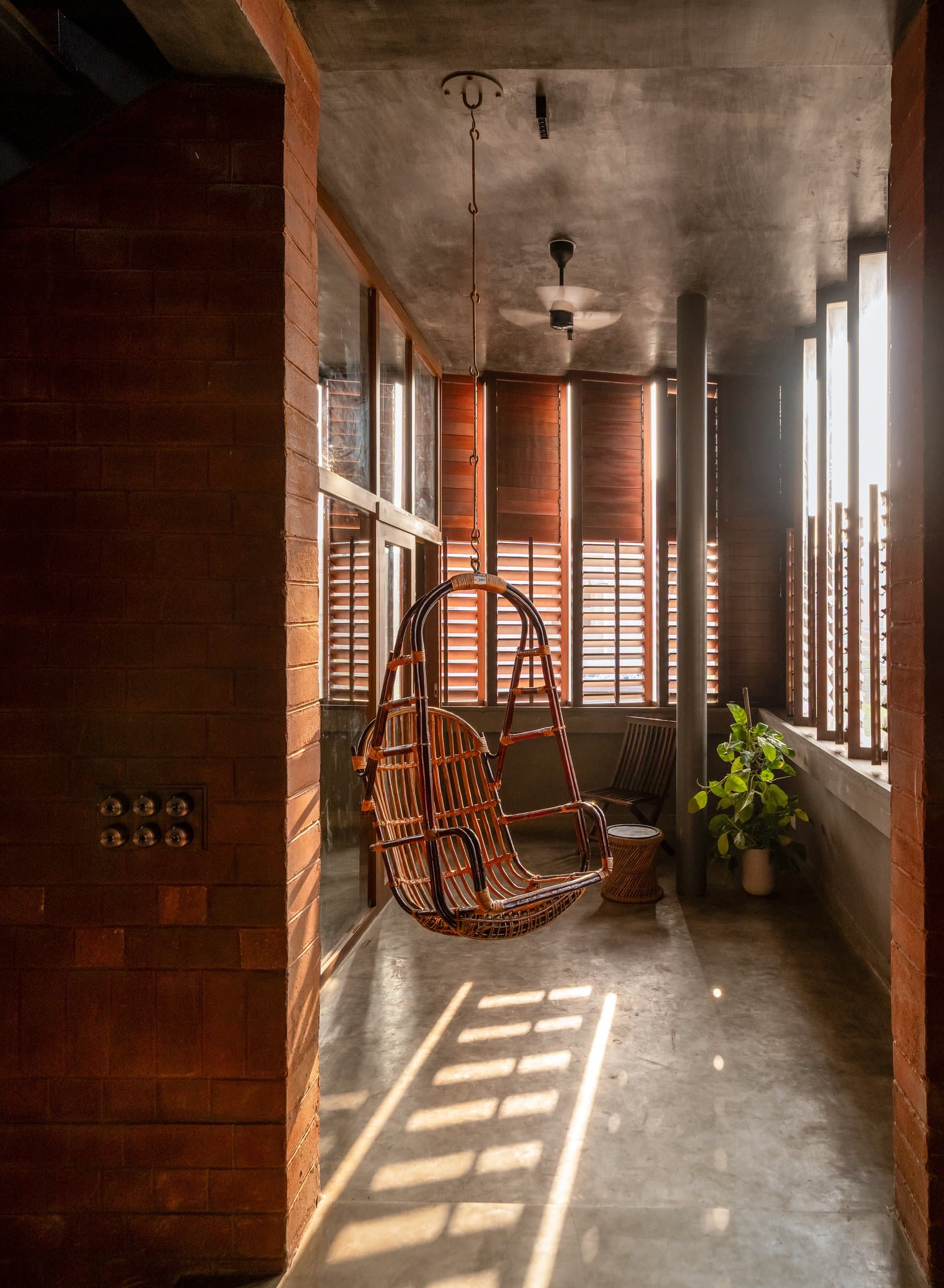 A cane hanging chair on the upper level, in a passage striped with light through timber louvers