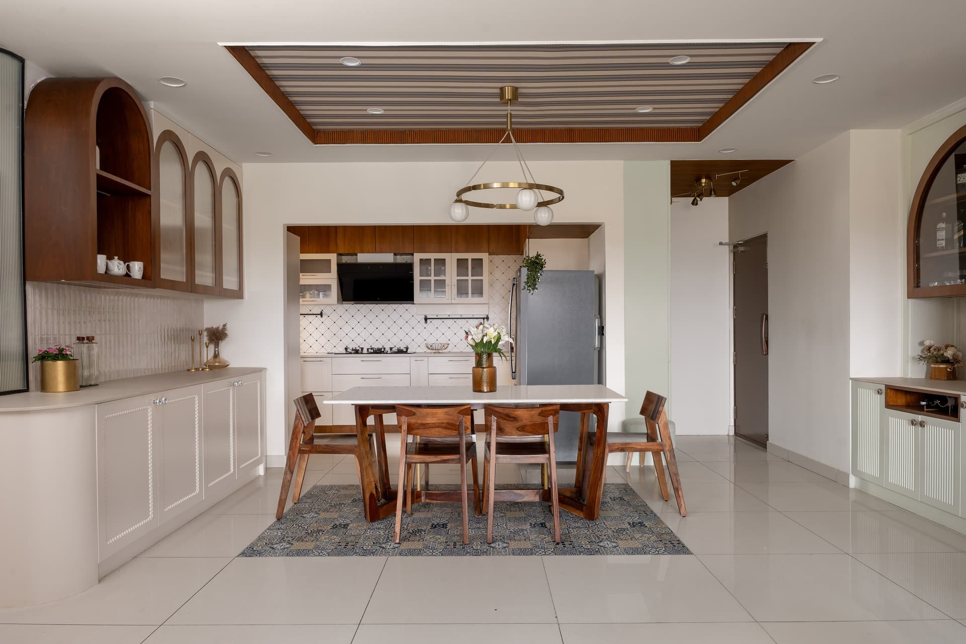 The full dining composition, where arched glass-fronted cabinets flank the table and the kitchen opens beyond