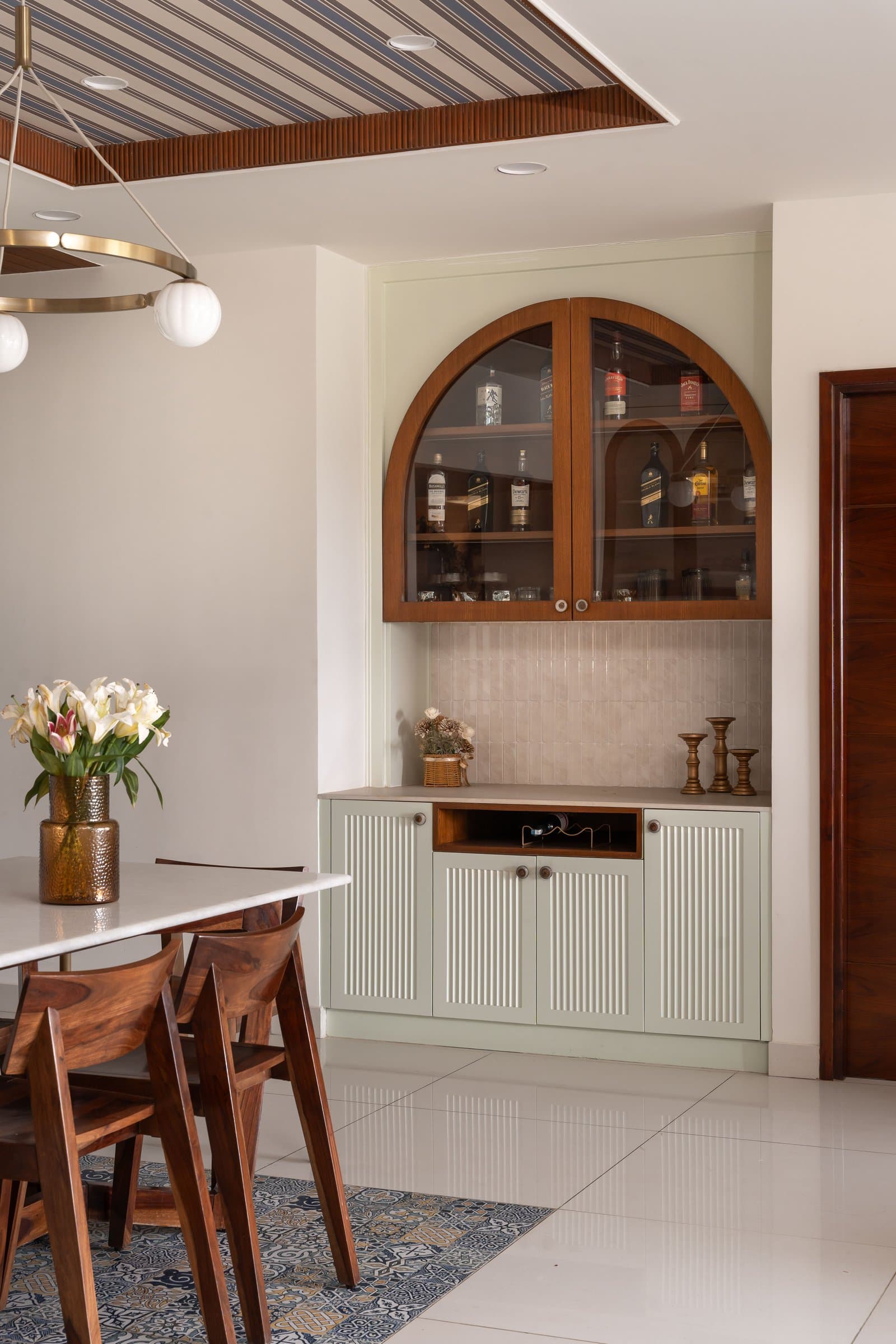 The bar niche in muted sage green, with fluted lower shutters and an arched glass upper cabinet