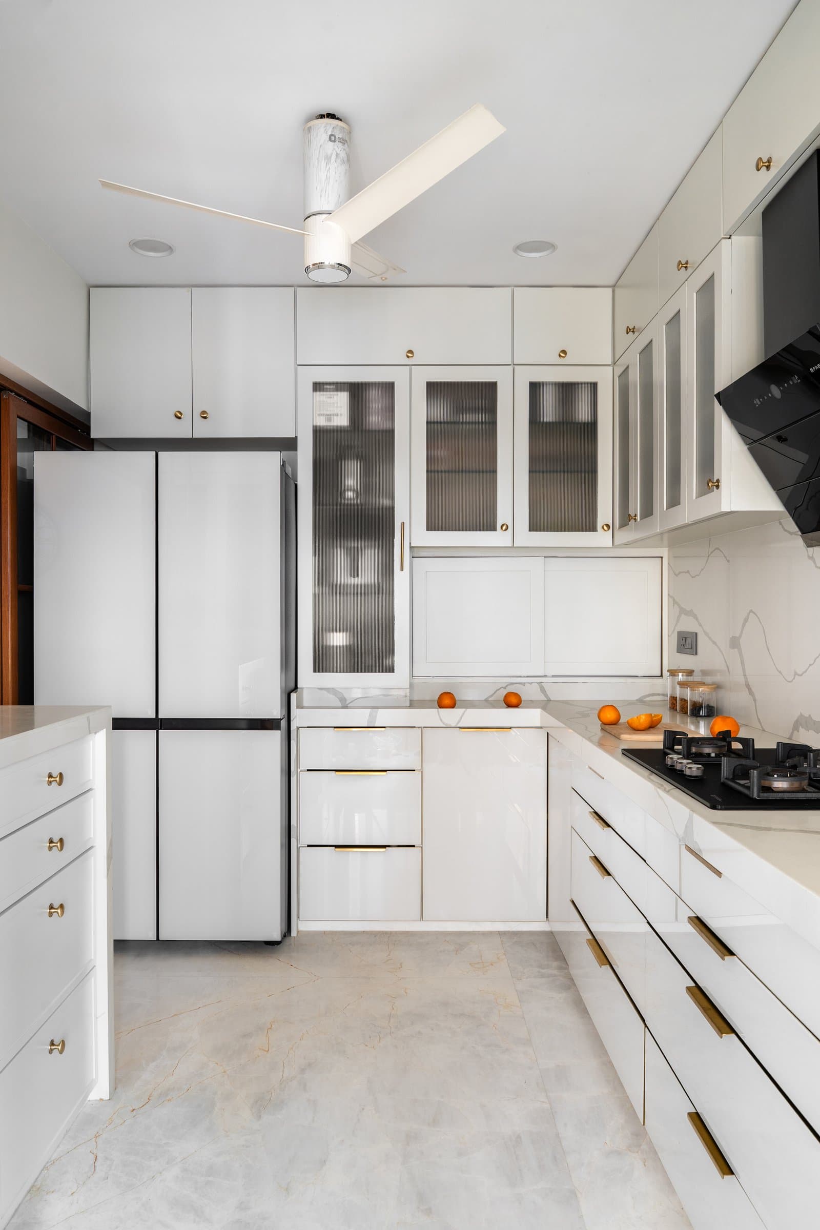 A deeper view of the compact L-shaped kitchen, organised around a tall pantry column and reeded-glass display cabinets