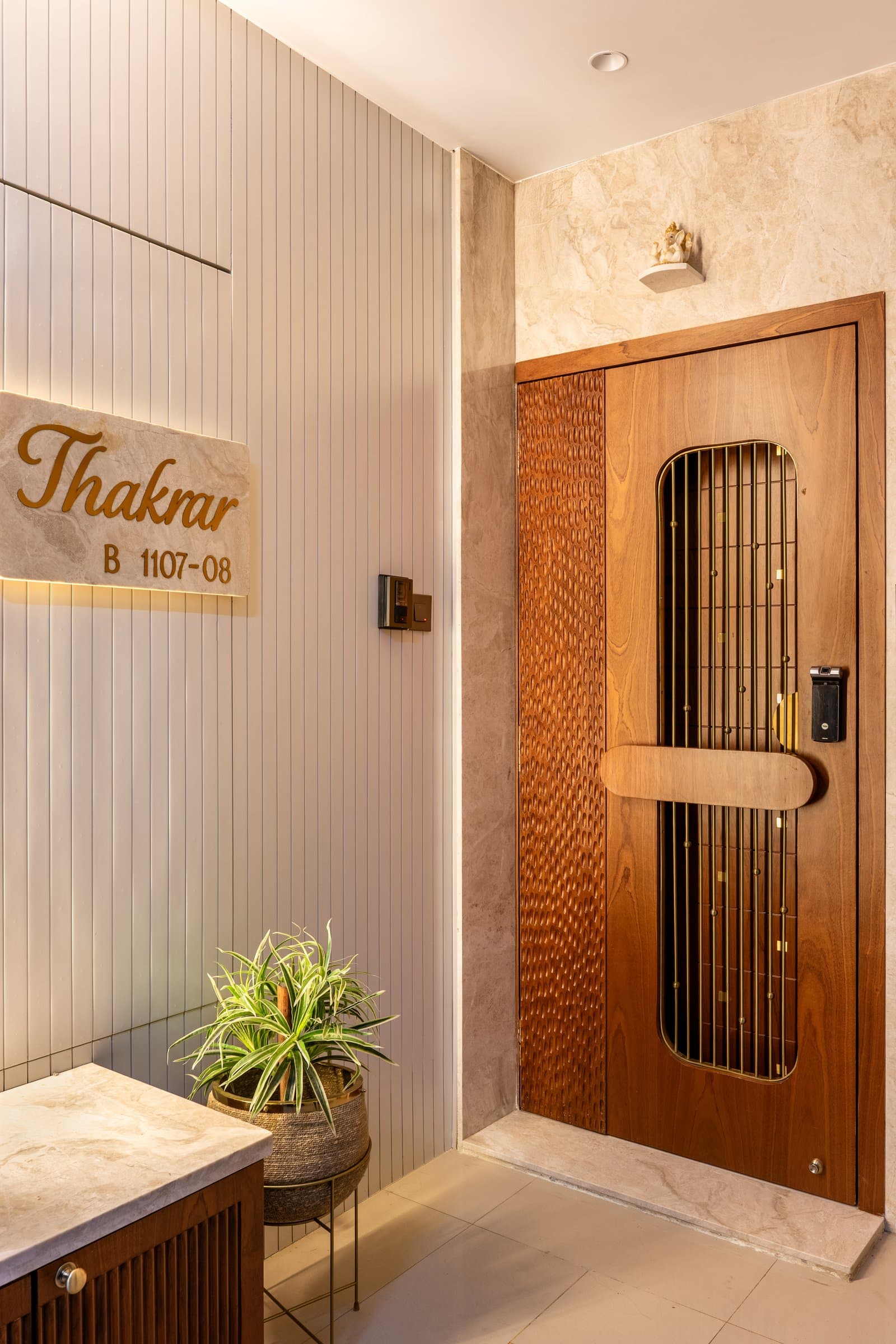 The entry, where a slatted ivory wall meets a warm stone-clad panel and a hammer-detailed teak front door