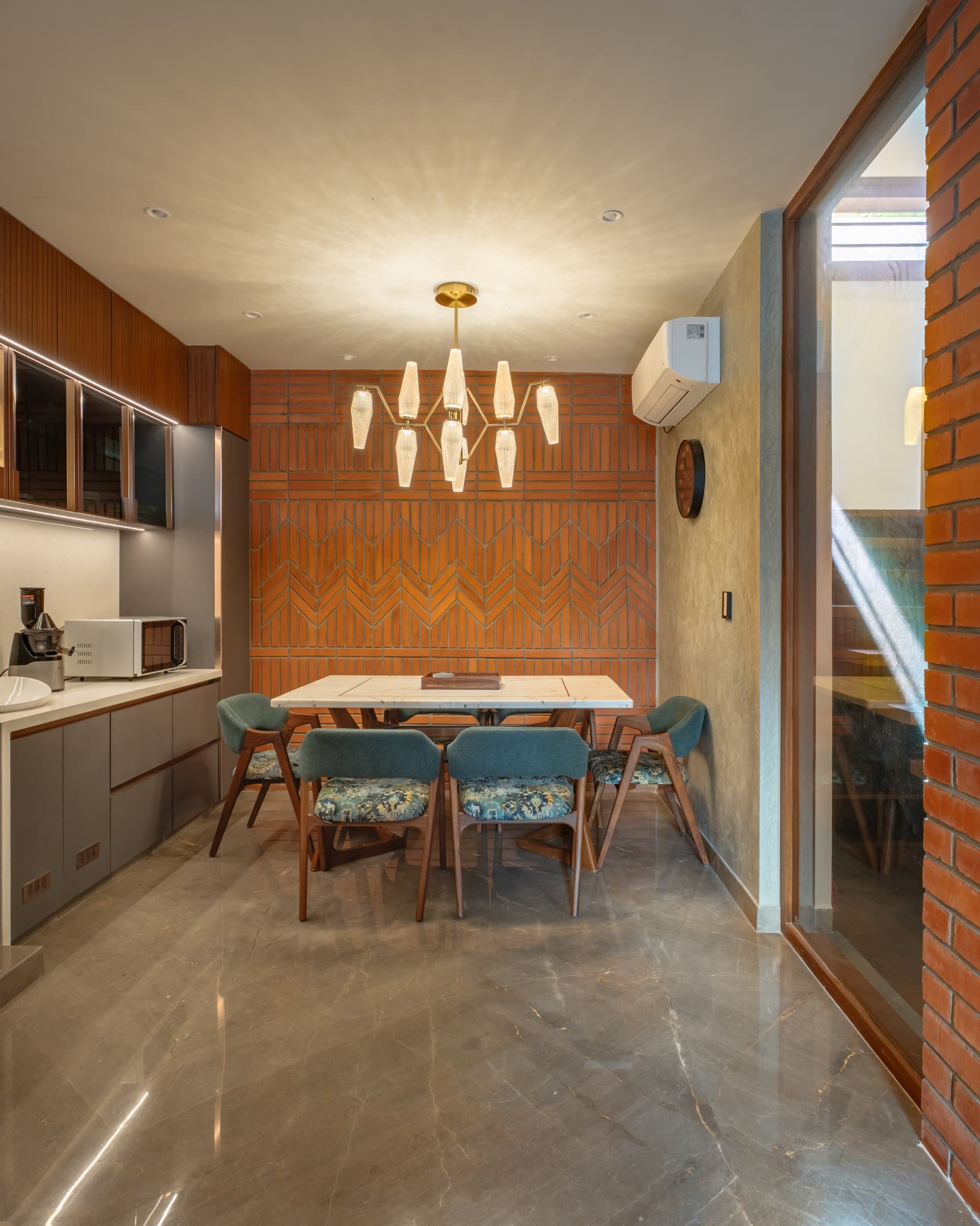 The dining area, where a herringbone-patterned brick feature wall sits beneath a clustered brass-and-glass chandelier