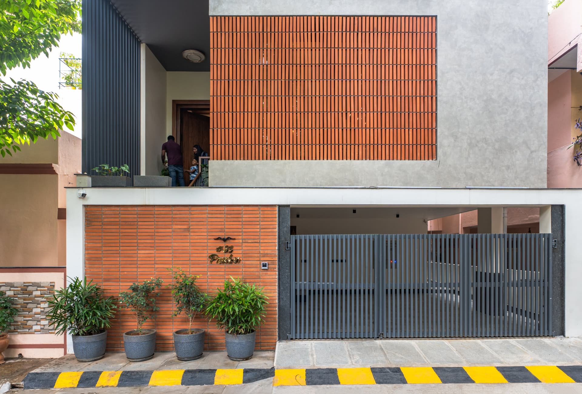 The street-facing elevation, where a ribbed terracotta band at ground level and a perforated brick screen above establish the home's material identity