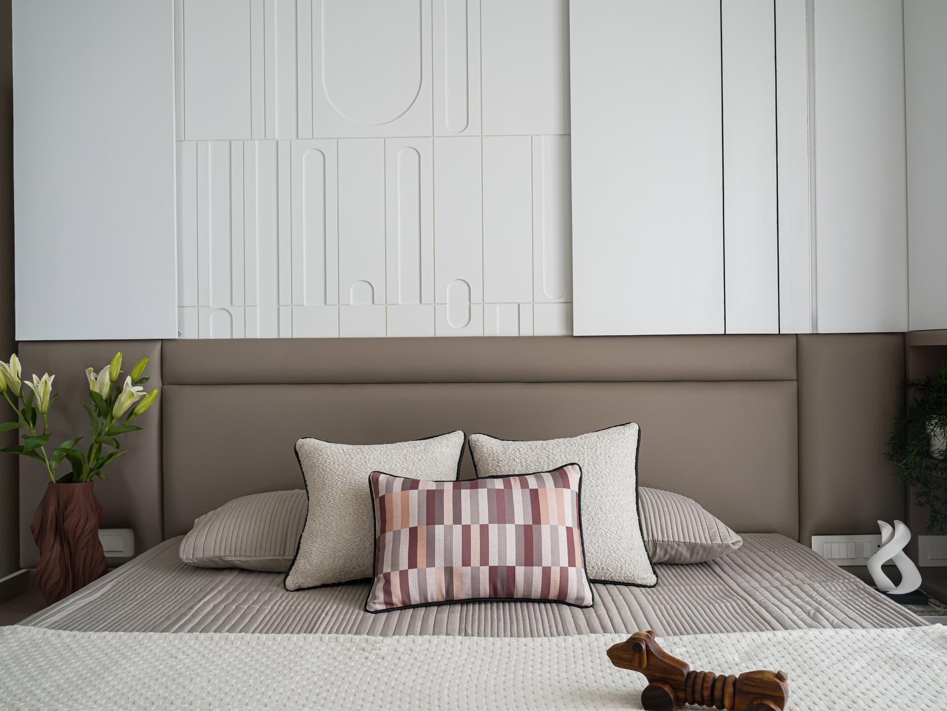 The primary bedroom, where a soft taupe upholstered headboard meets a sculpted white relief panel above