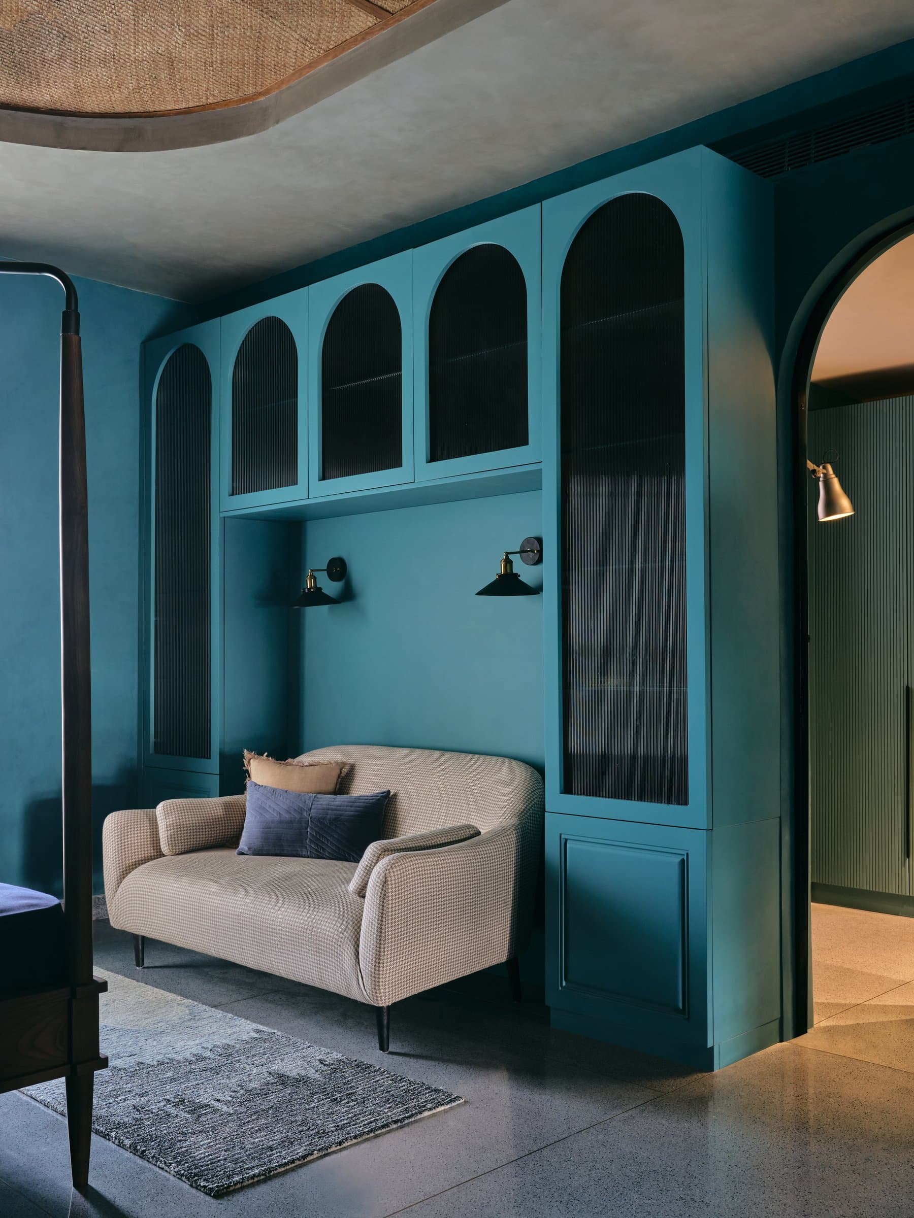 The adjoining nook, where reeded-glass arched cabinetry in deep teal meets a small houndstooth sofa