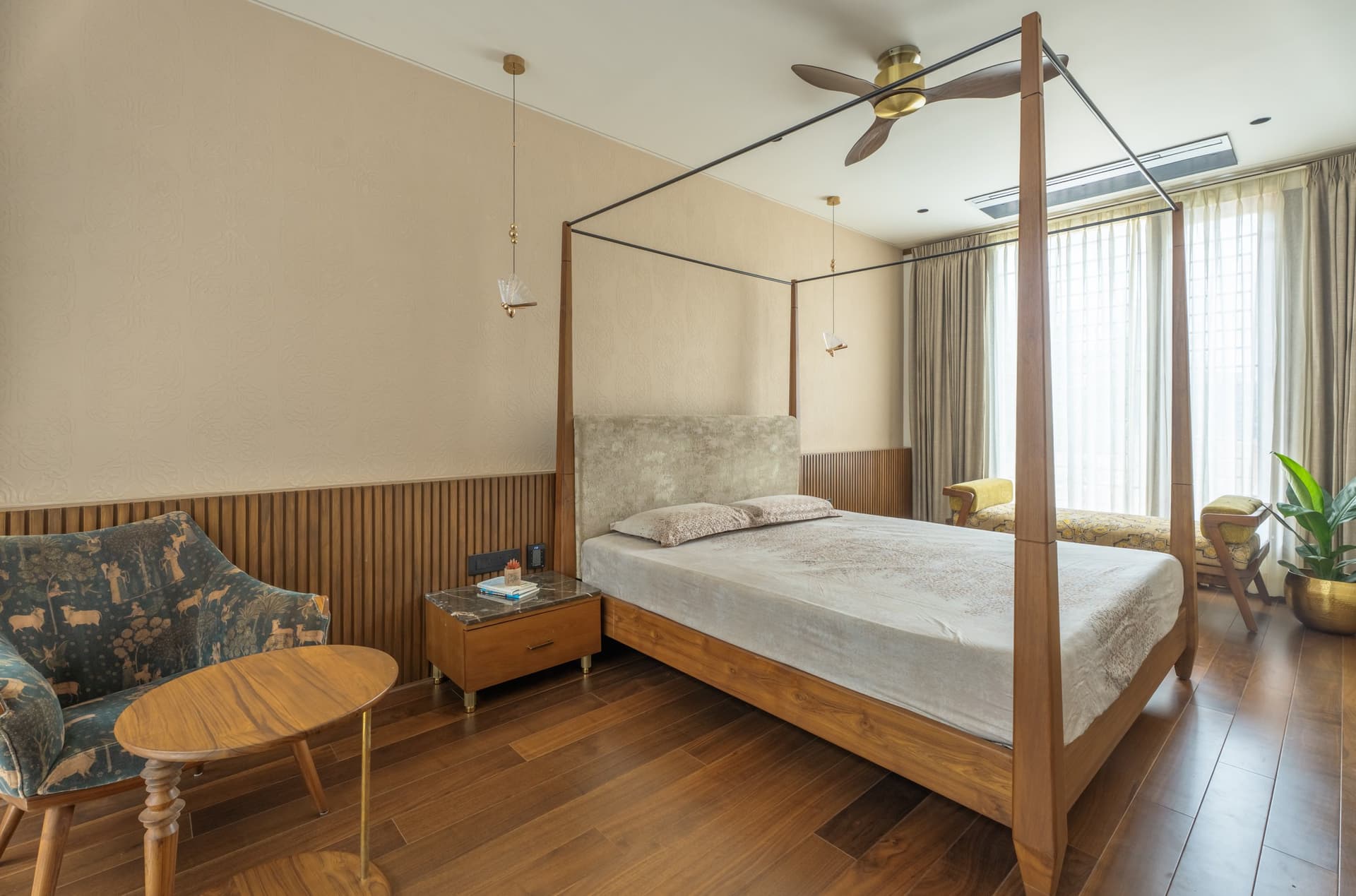 The primary bedroom, where a four-poster teak bed sits against vertical timber wainscoting and a pale patterned wall