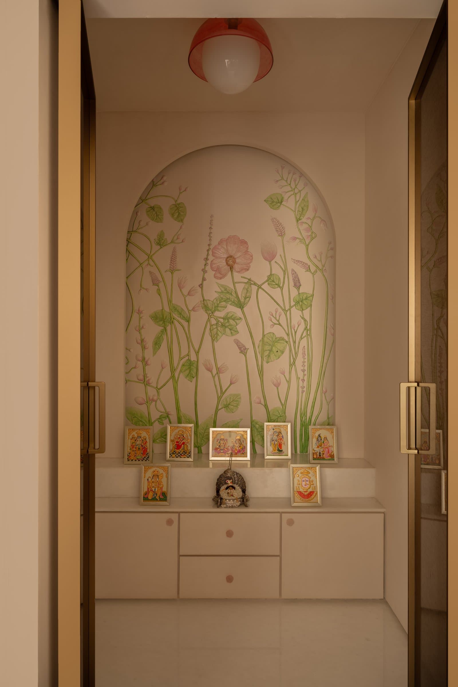 The pooja niche, where a hand-painted botanical arch frames a gathering of miniature devotional works