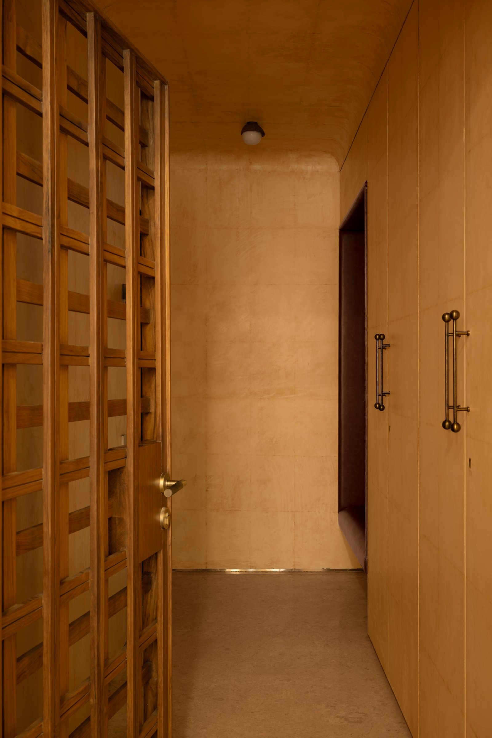 The entry, where a latticed teak door and leather-clad joinery establish the home's tactile grammar before the interior fully reveals itself