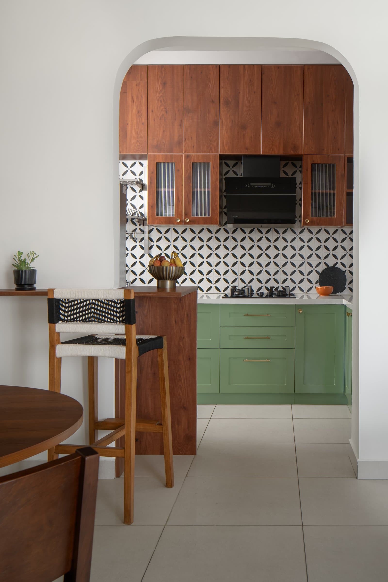 The kitchen, framed by an arch, pairs warm hardwood uppers with sage green lower cabinets and a patterned tile backsplash