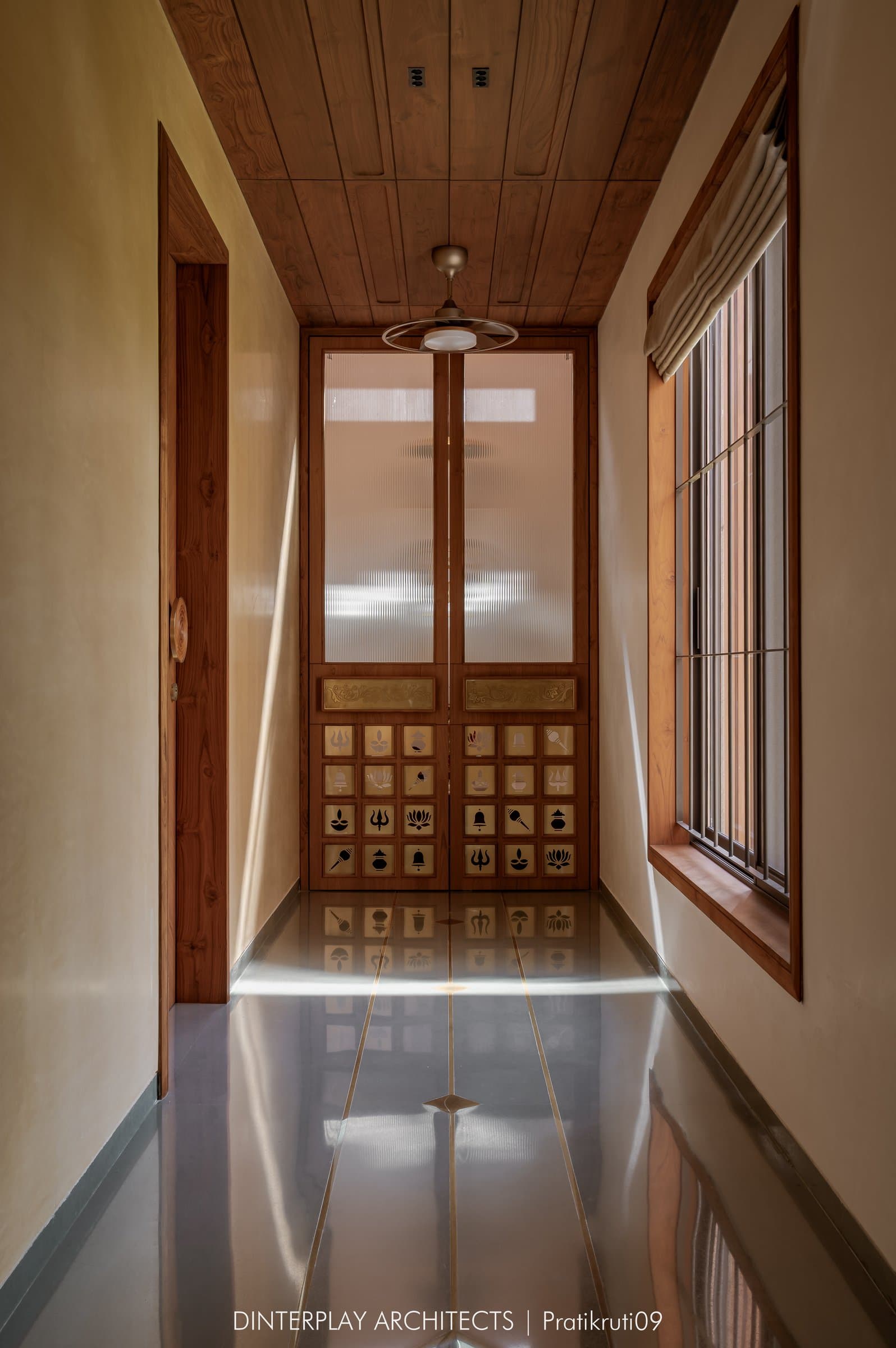 The mandir passage, where warm ochre walls and a brass-inlaid floor lead to reeded-glass devotional doors
