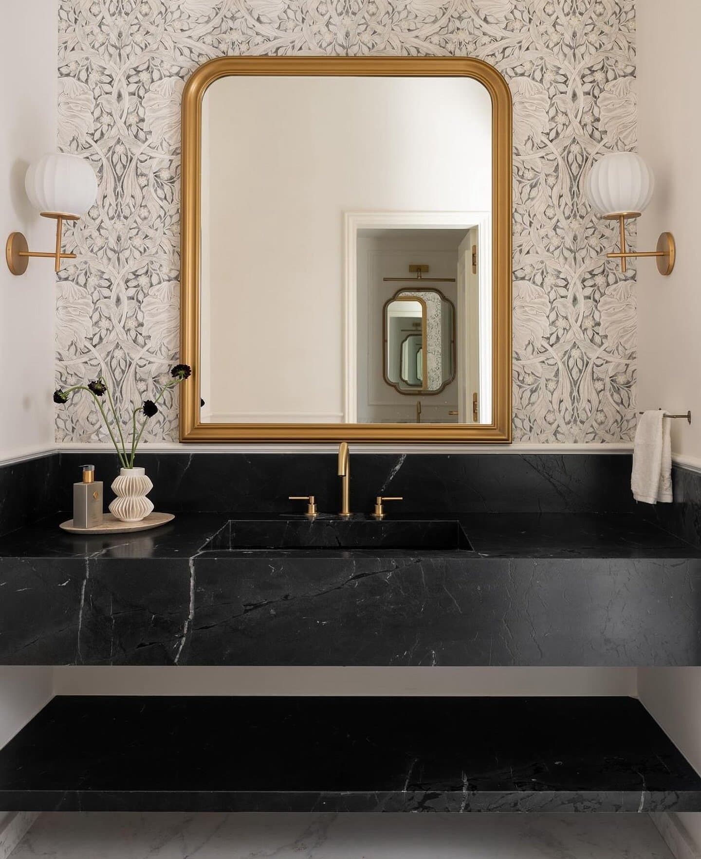 The powder room's arched mirror, black marble slab, and brushed brass fittings.