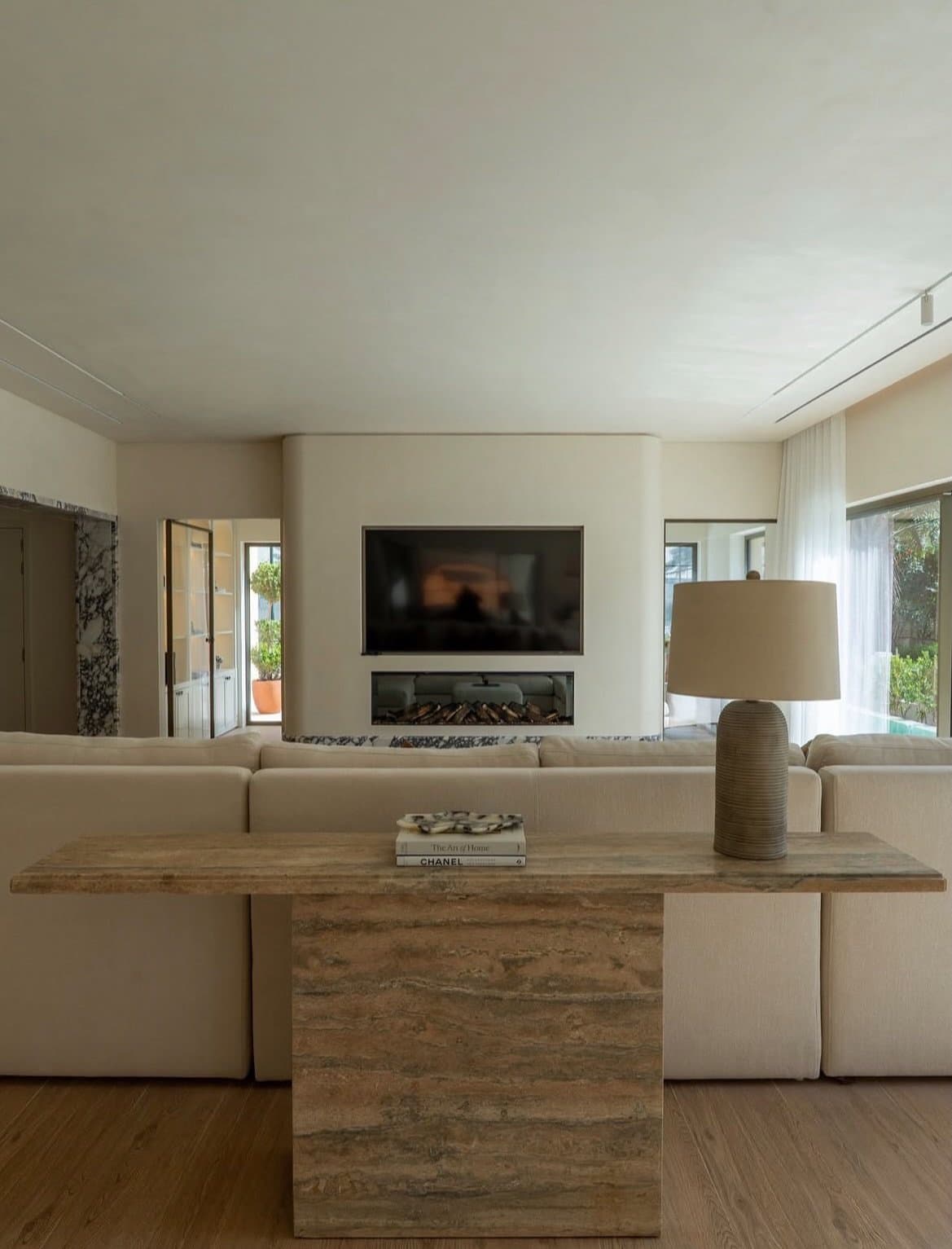 A curved plaster wall organises the living room around a recessed fireplace and bookmatched travertine console.