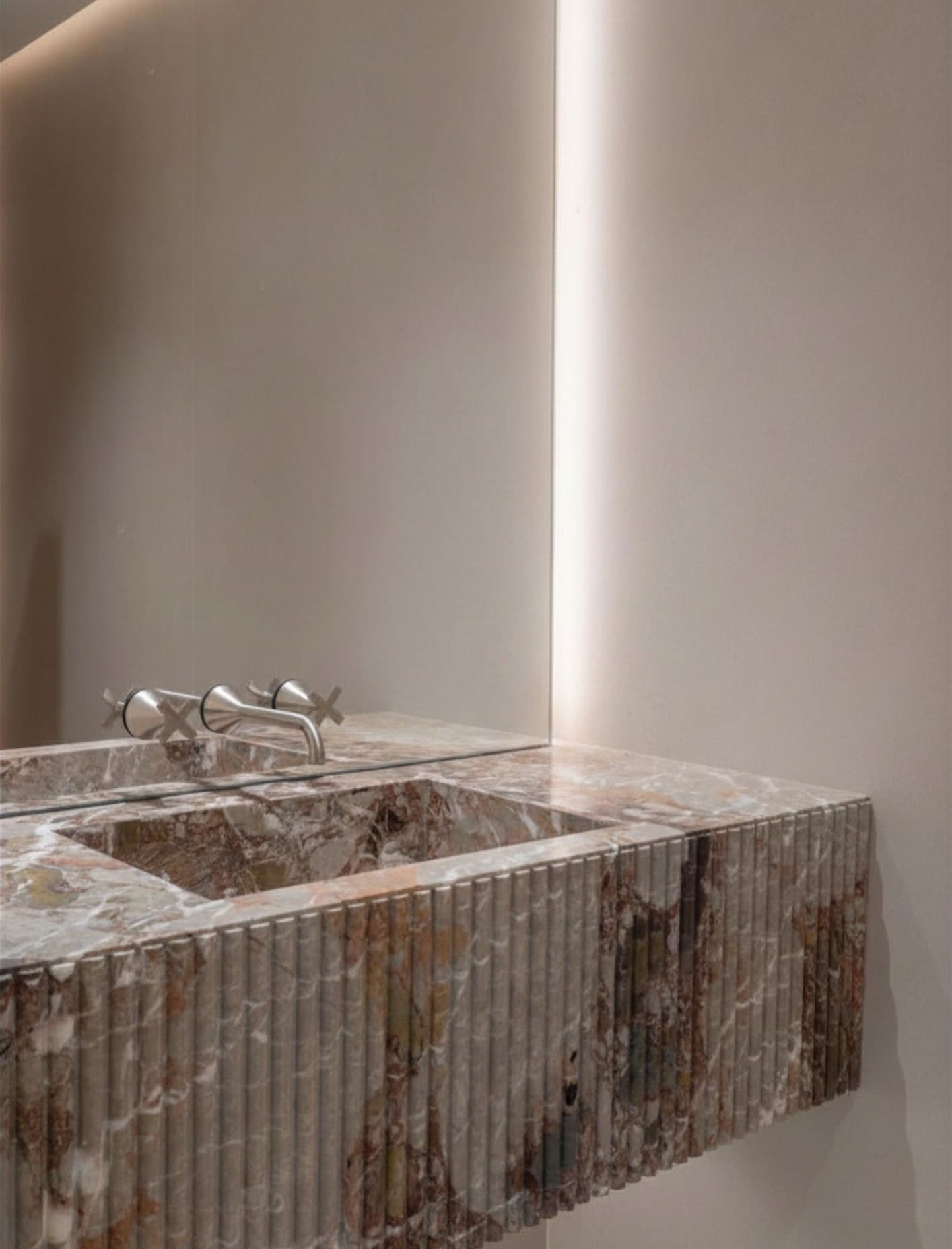 A fluted stone vanity edge catches light in narrow vertical ribs against soft plaster.