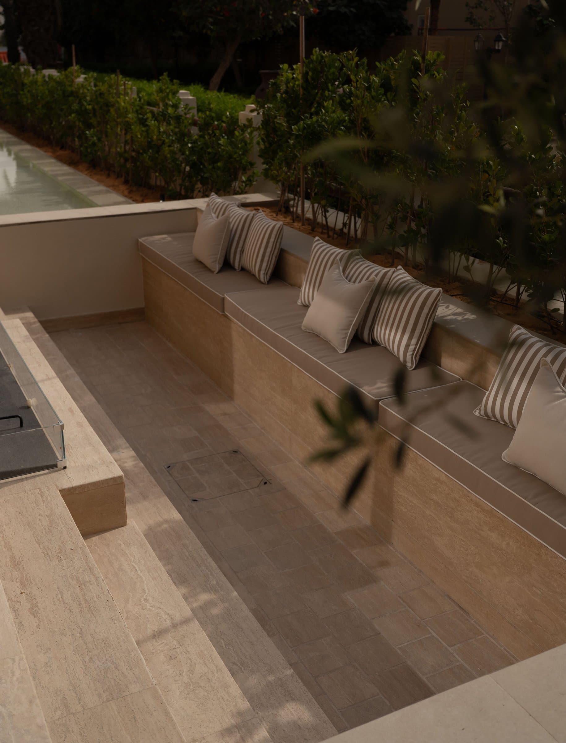A sunken garden nook lined with stone benches and striped cushions, held within a green enclosure.