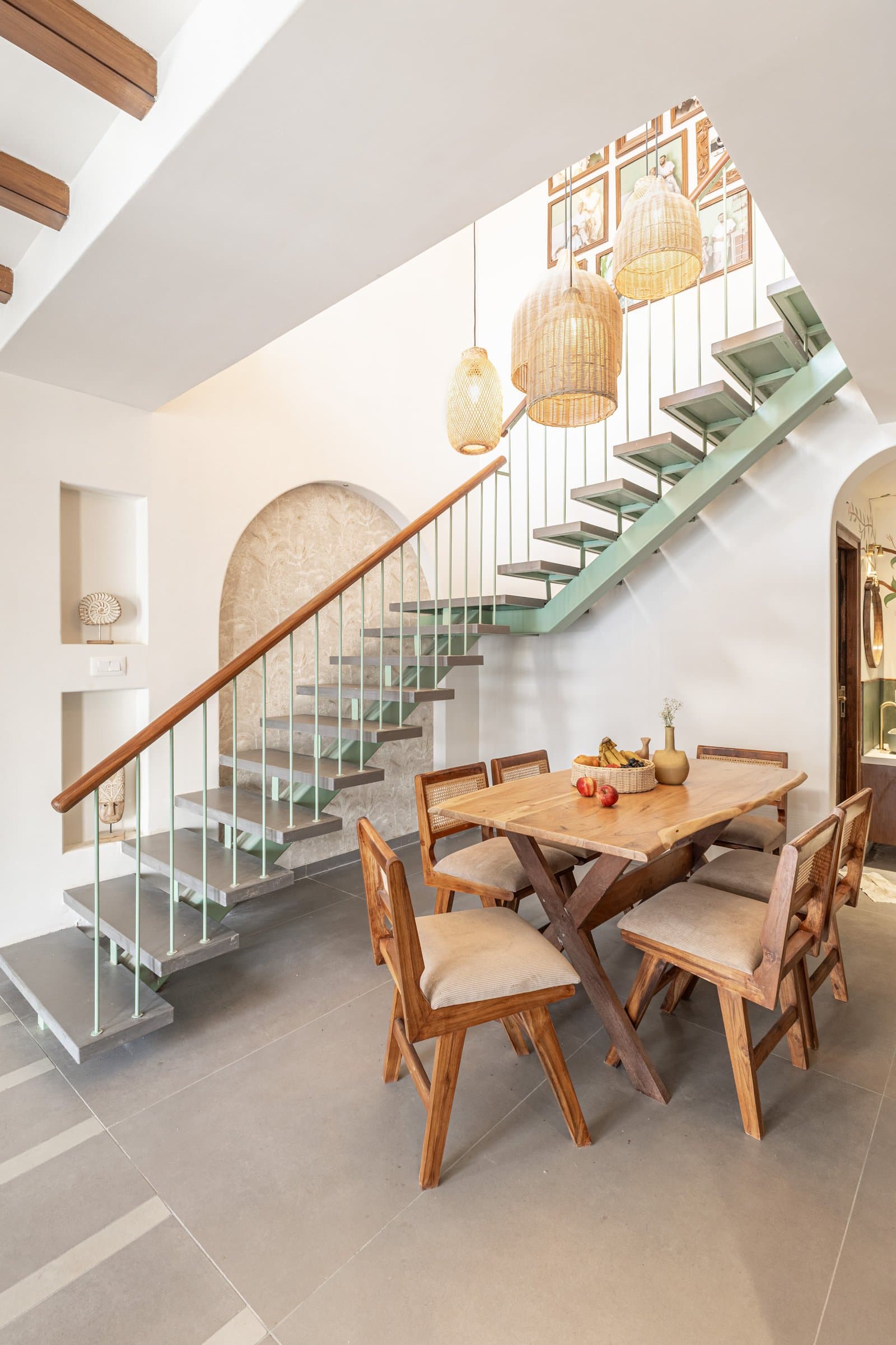 The dining area beneath the stair, where three woven cane pendants descend as a sculptural cluster