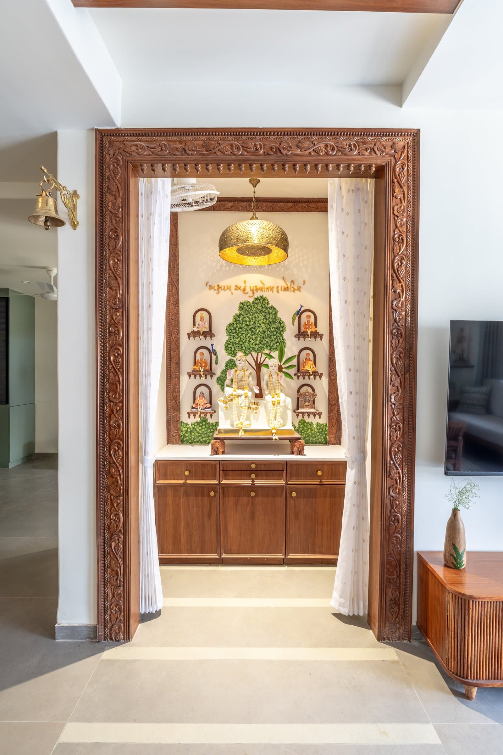 The mandir seen directly, its marble shrine backed by hand-painted foliage and lit by a perforated brass pendant