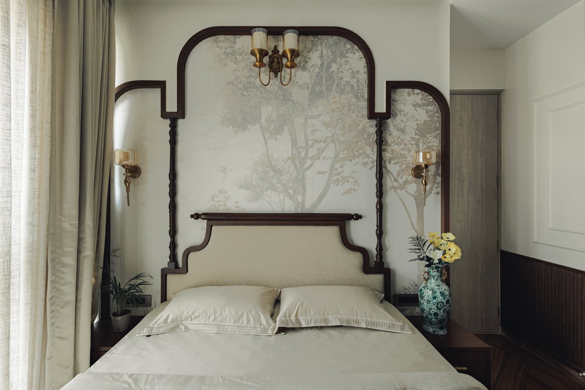 The master bedroom, where a curved walnut headboard and botanical mural are framed by turned spindles and brass sconces