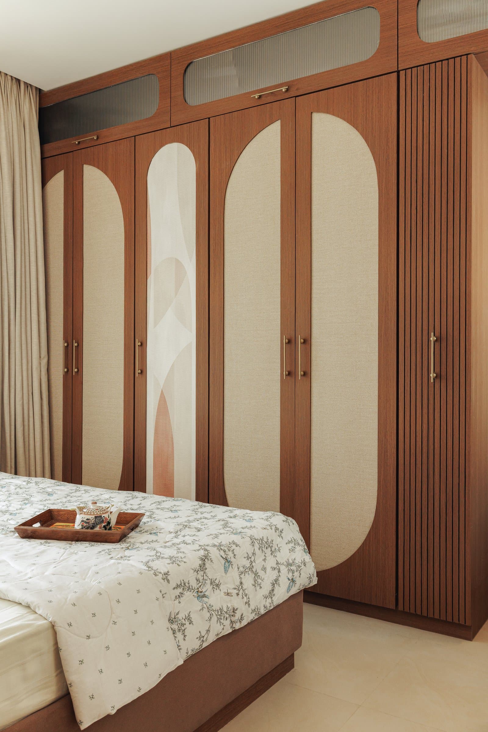 The wardrobe wall in warm timber, inset with oatmeal fabric panels and a graphic curved motif