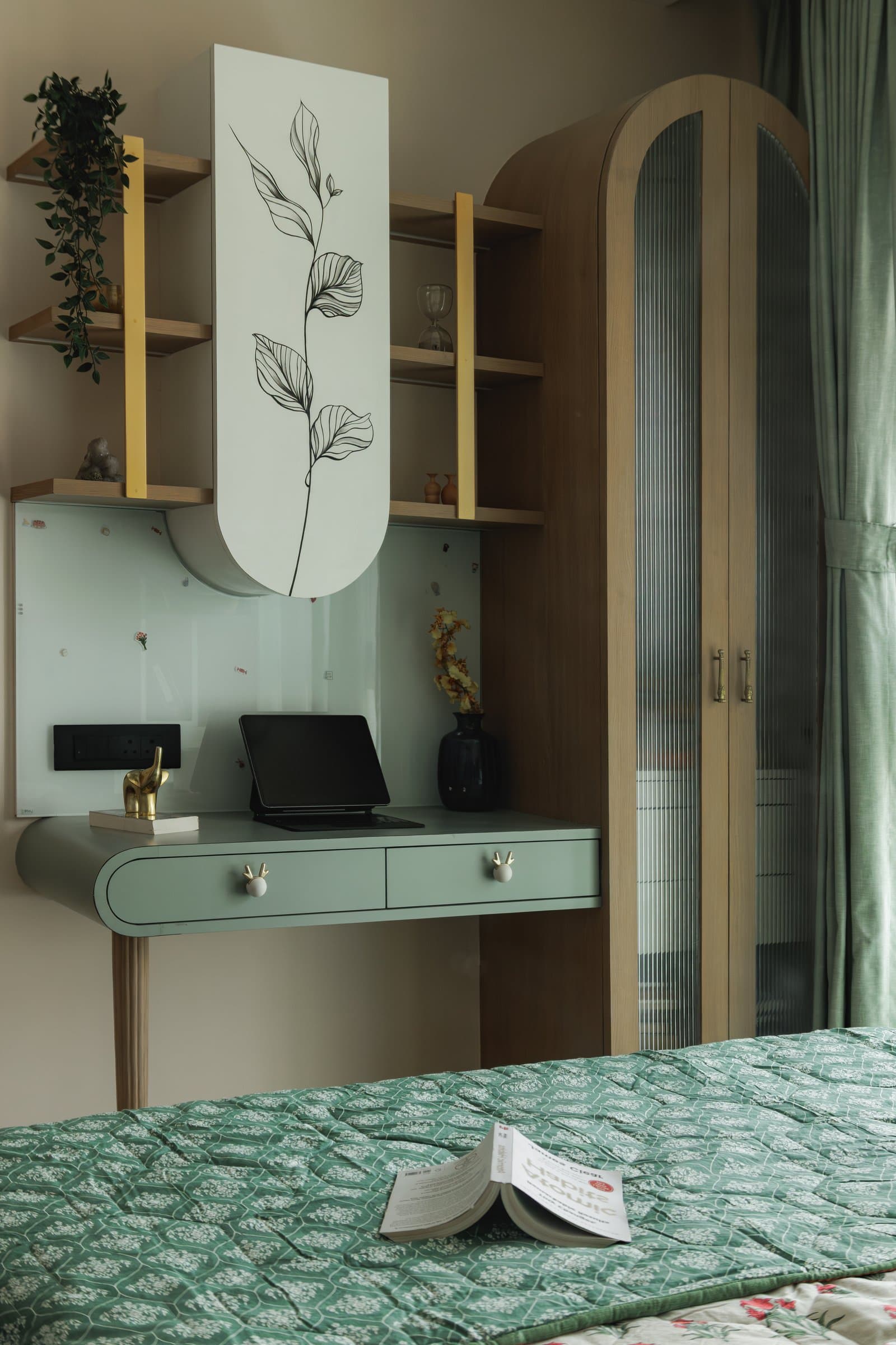 The dressing corner in muted sage green, with a curved desk and a fluted glass wardrobe alongside