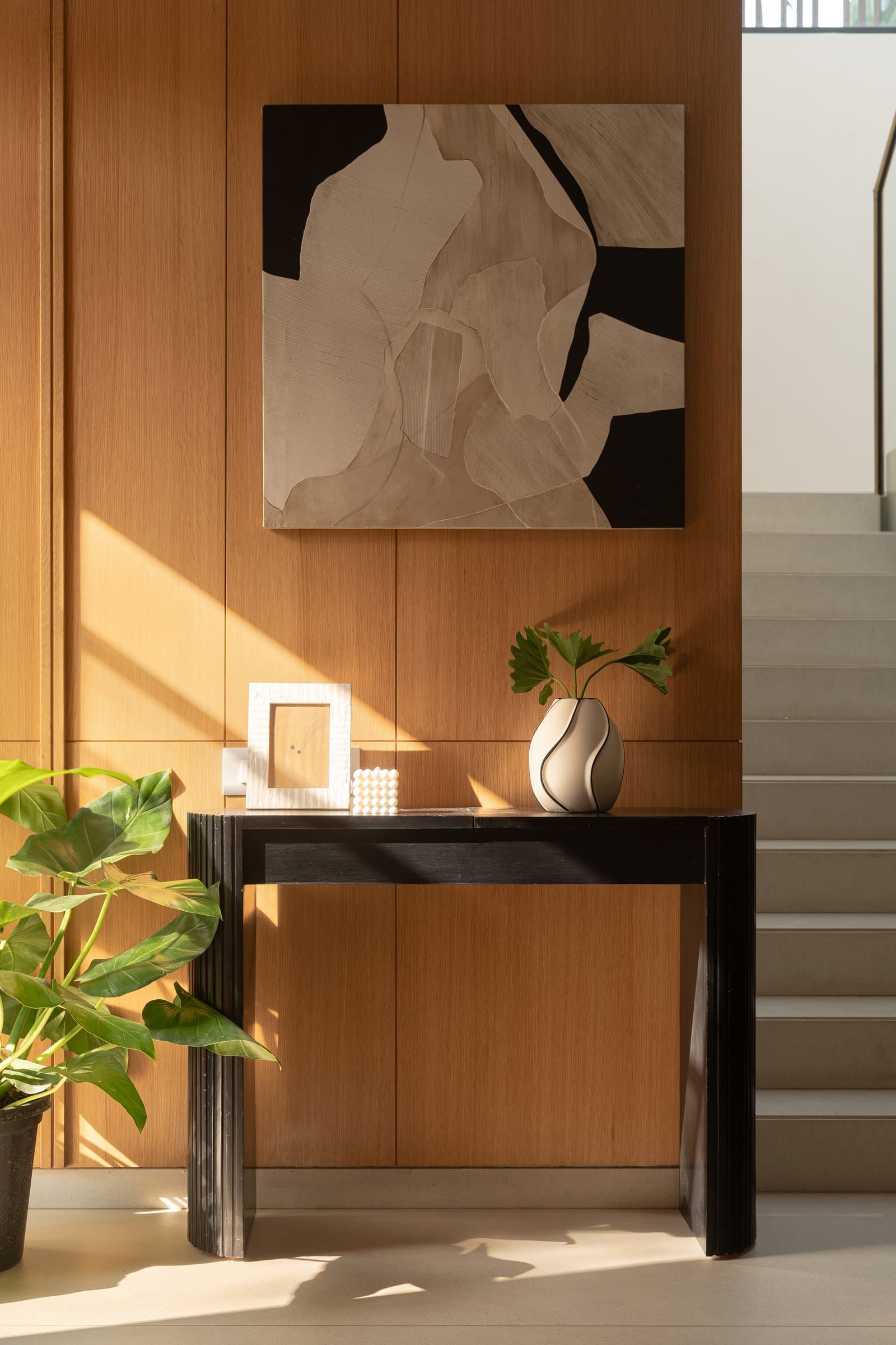 The foyer, where a warm timber wall holds an abstract composition above a dark fluted console