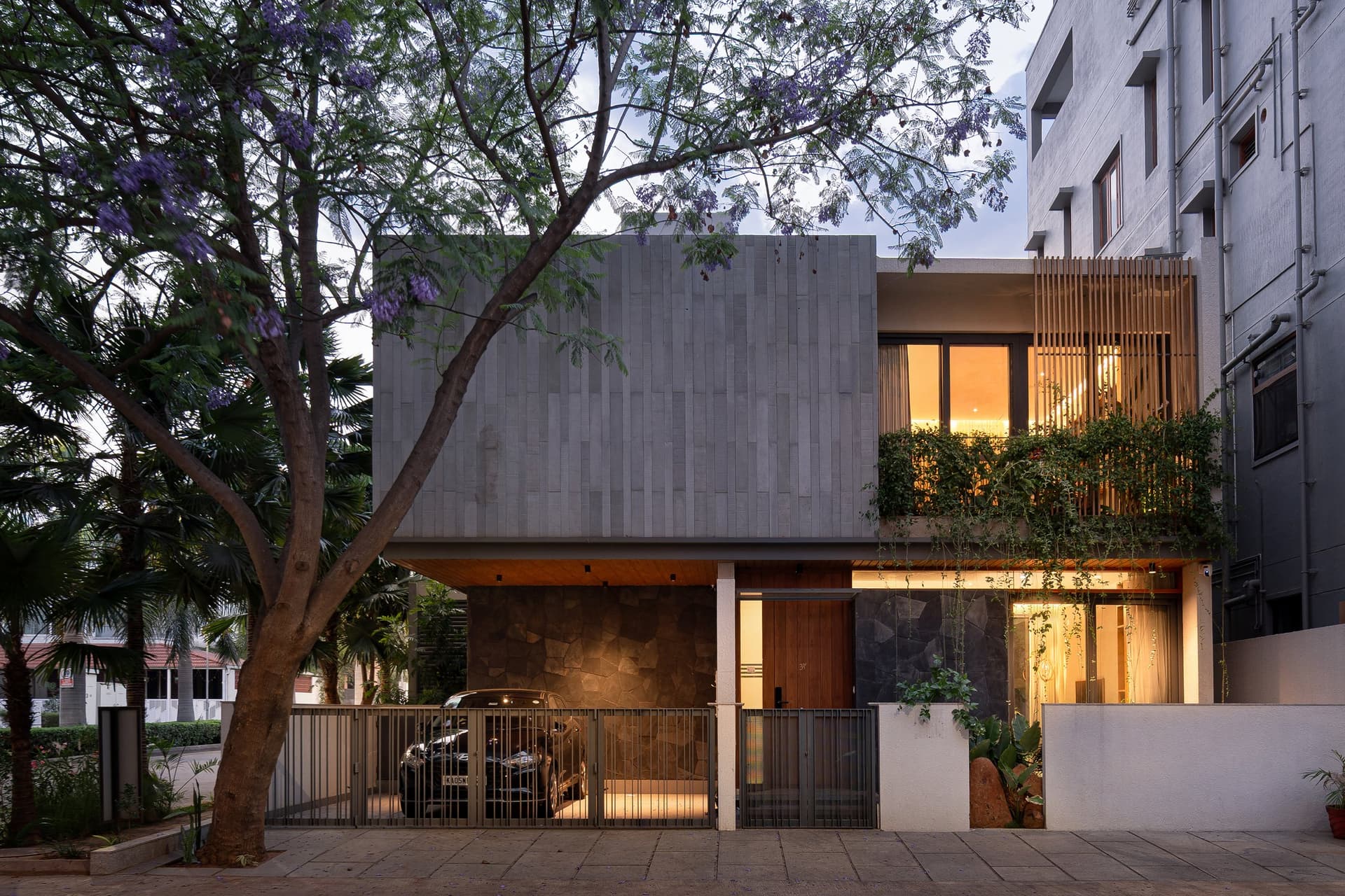 The residence, seen at dusk, its upper volume of vertically banded stone cladding set above a ground floor of timber and rough stone