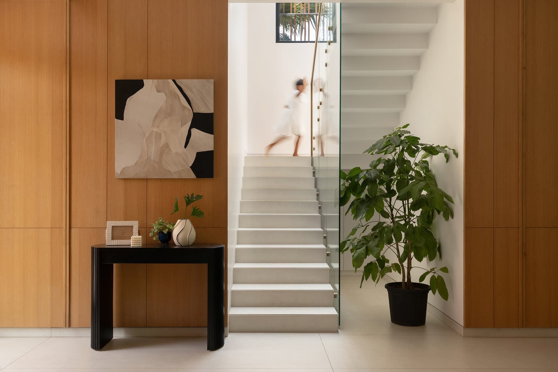 The staircase, lifted behind a frameless glass balustrade and lit by daylight from above