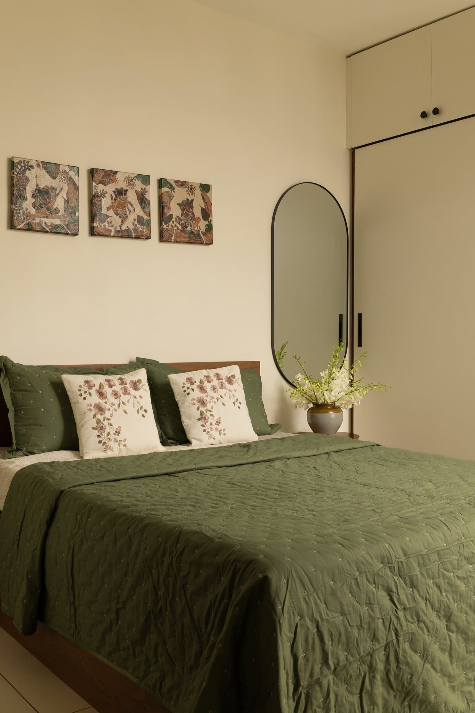 The master bedroom, where a trio of figurative artworks and a slim oval mirror balance the pale wardrobe beside the bed
