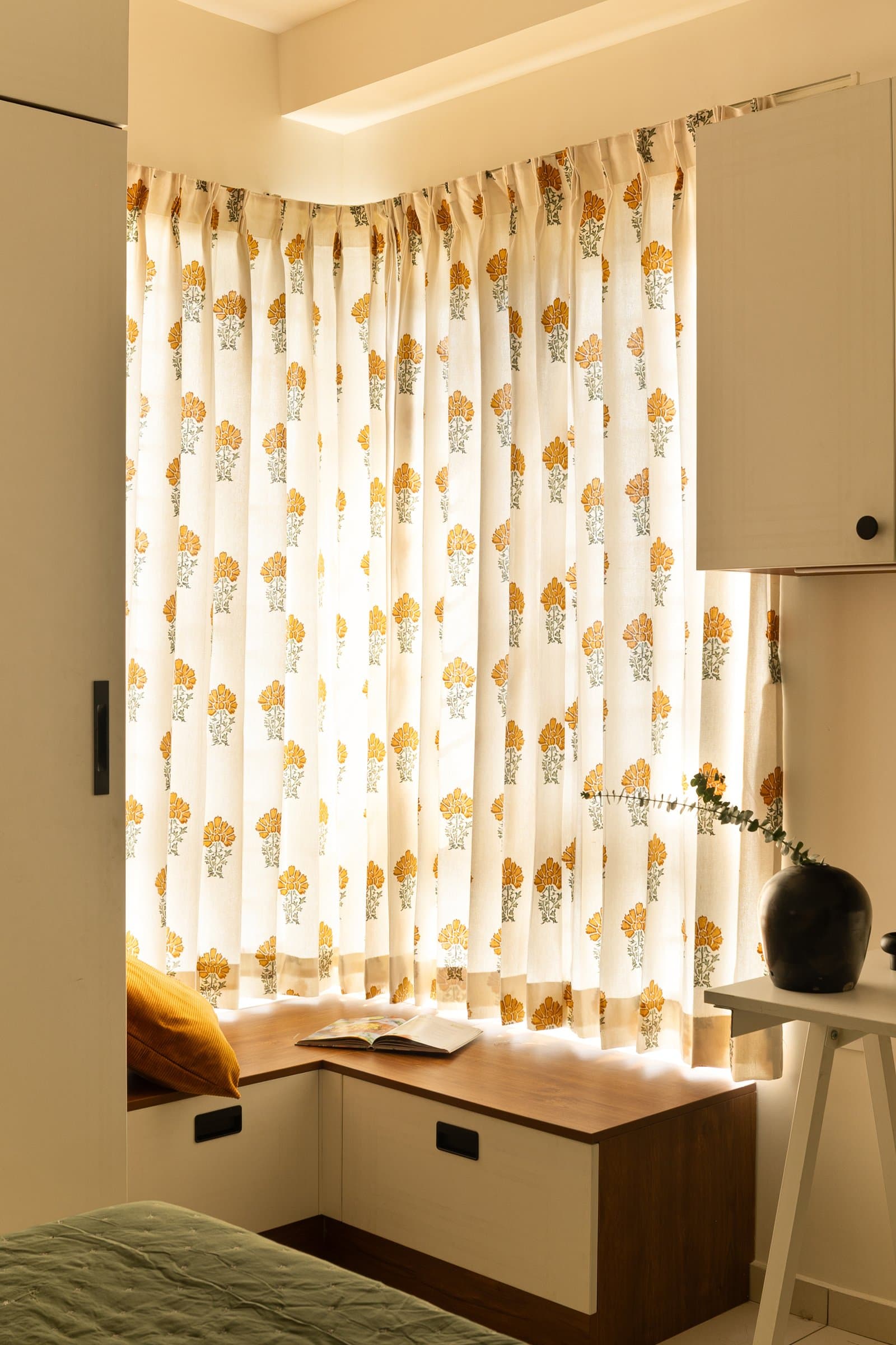 The window seat in fuller light, a block-print curtain filtering the afternoon into the compact room