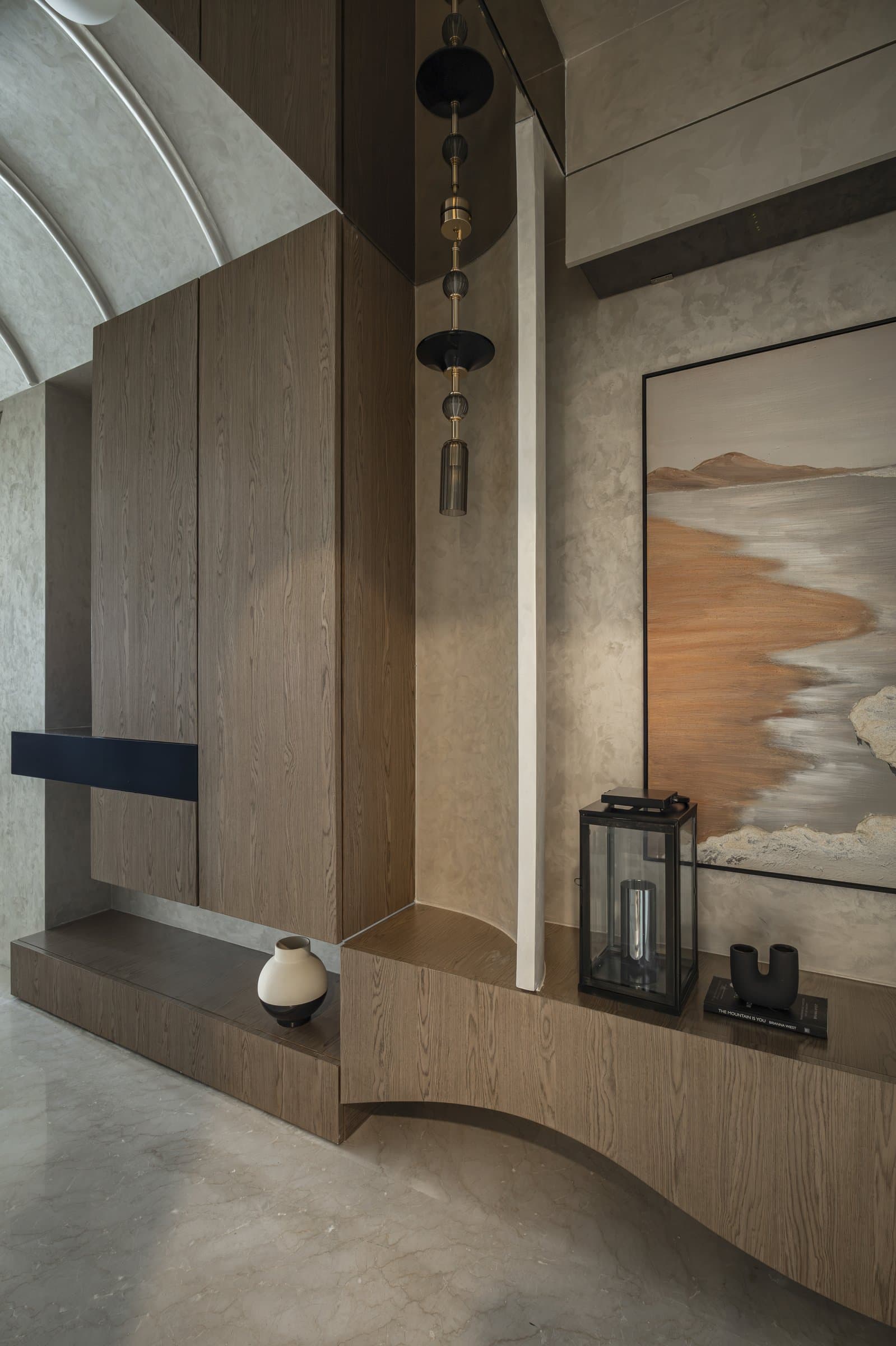A vaulted passage holding a veneered console with a tiered pendant of blackened discs and brass