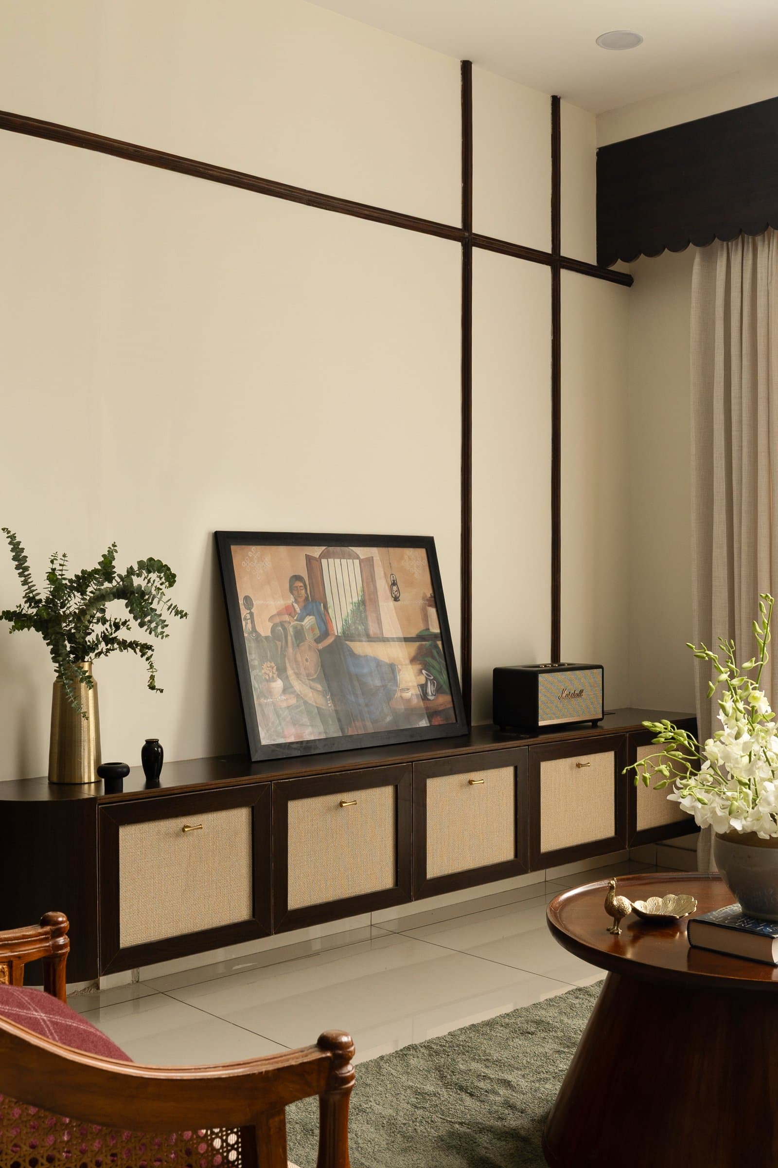 The console wall, where a crossed grid of dark trim frames a cane-fronted sideboard and a leaning framed work