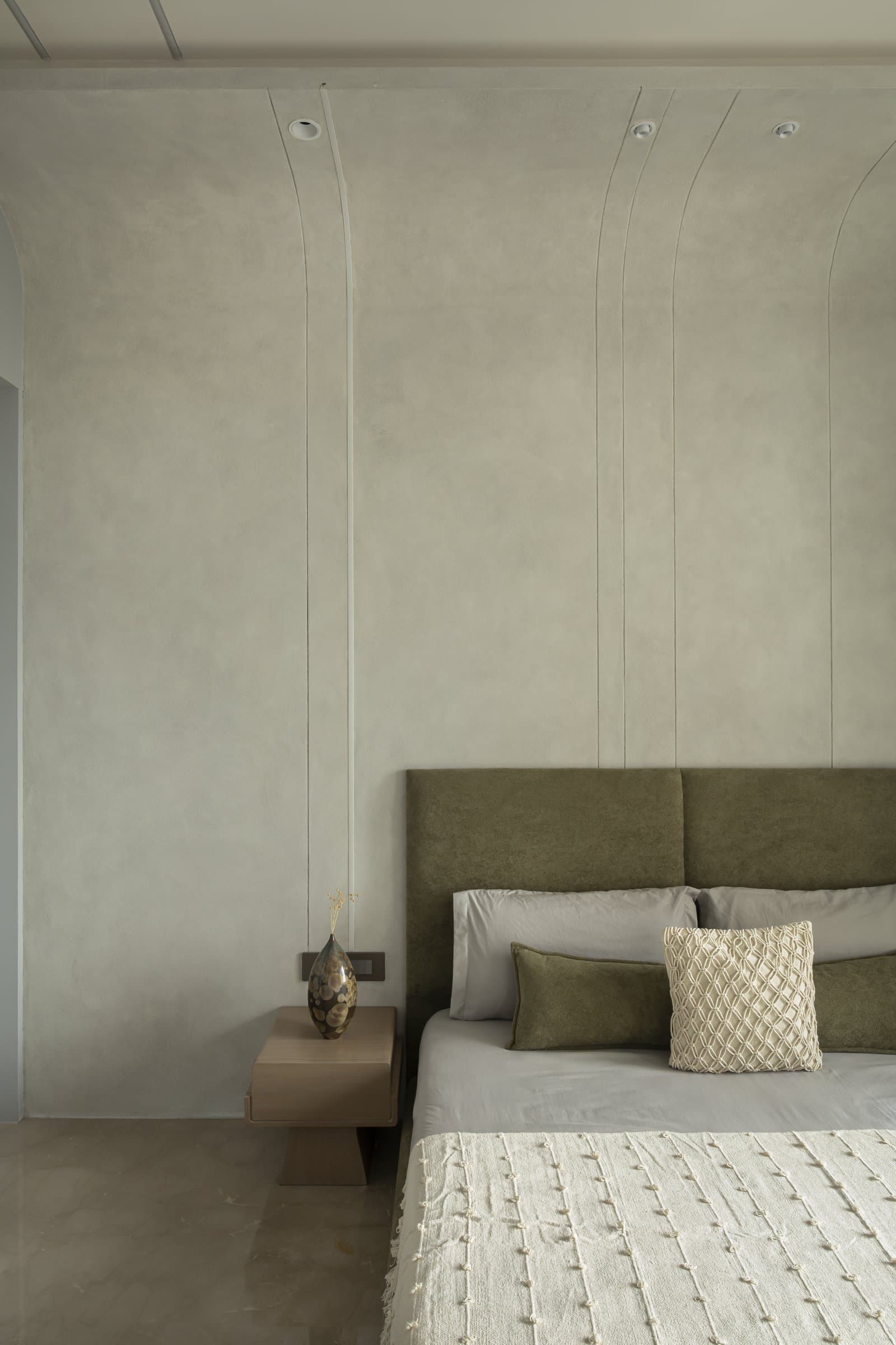 The third bedroom's textured plaster wall, with vertical reveals rising into the ceiling behind a deep olive headboard