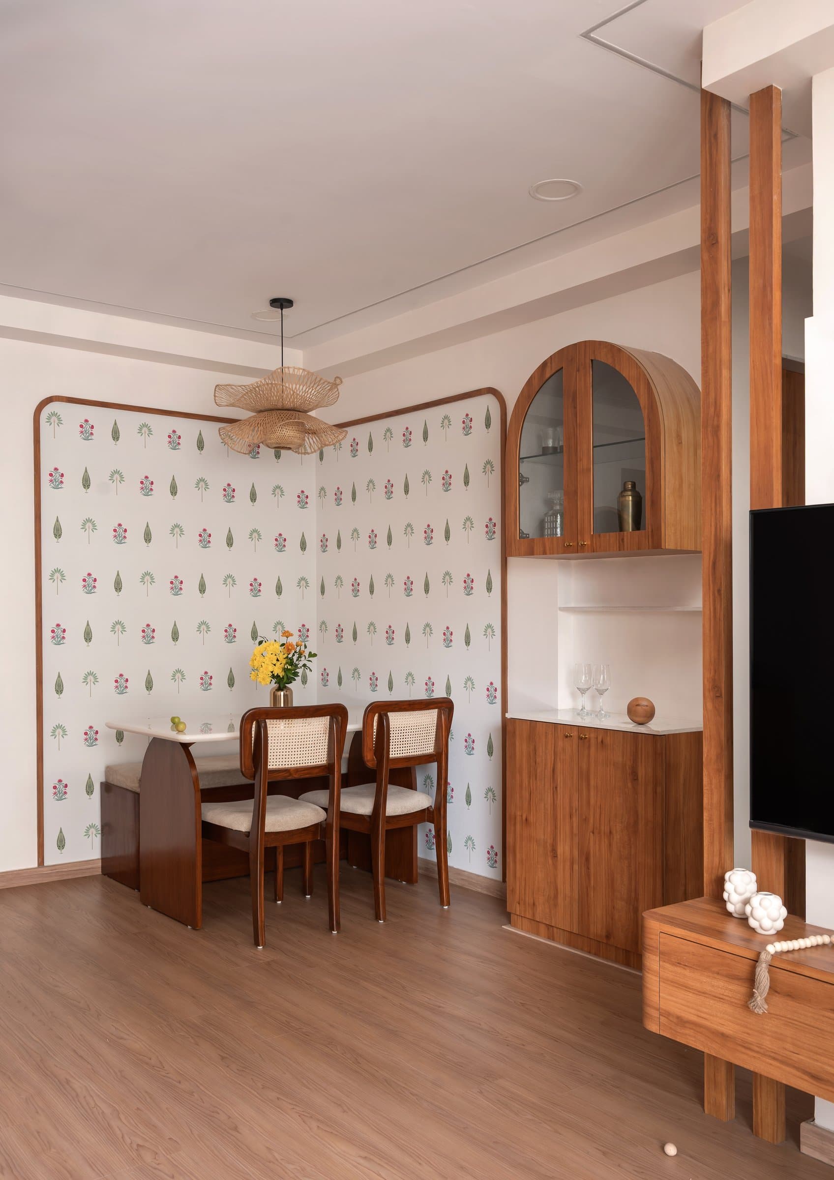 The dining nook, where a patterned wallpaper sits within a rounded wooden frame beside a woven pendant