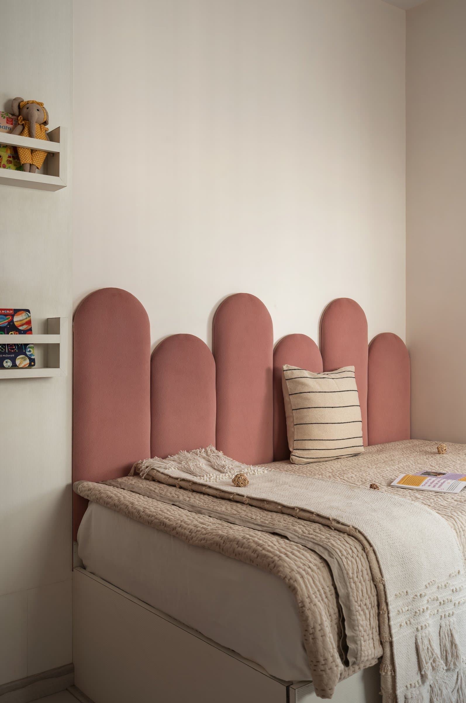 An upholstered headboard of rounded panels in dusty rose anchors the bed