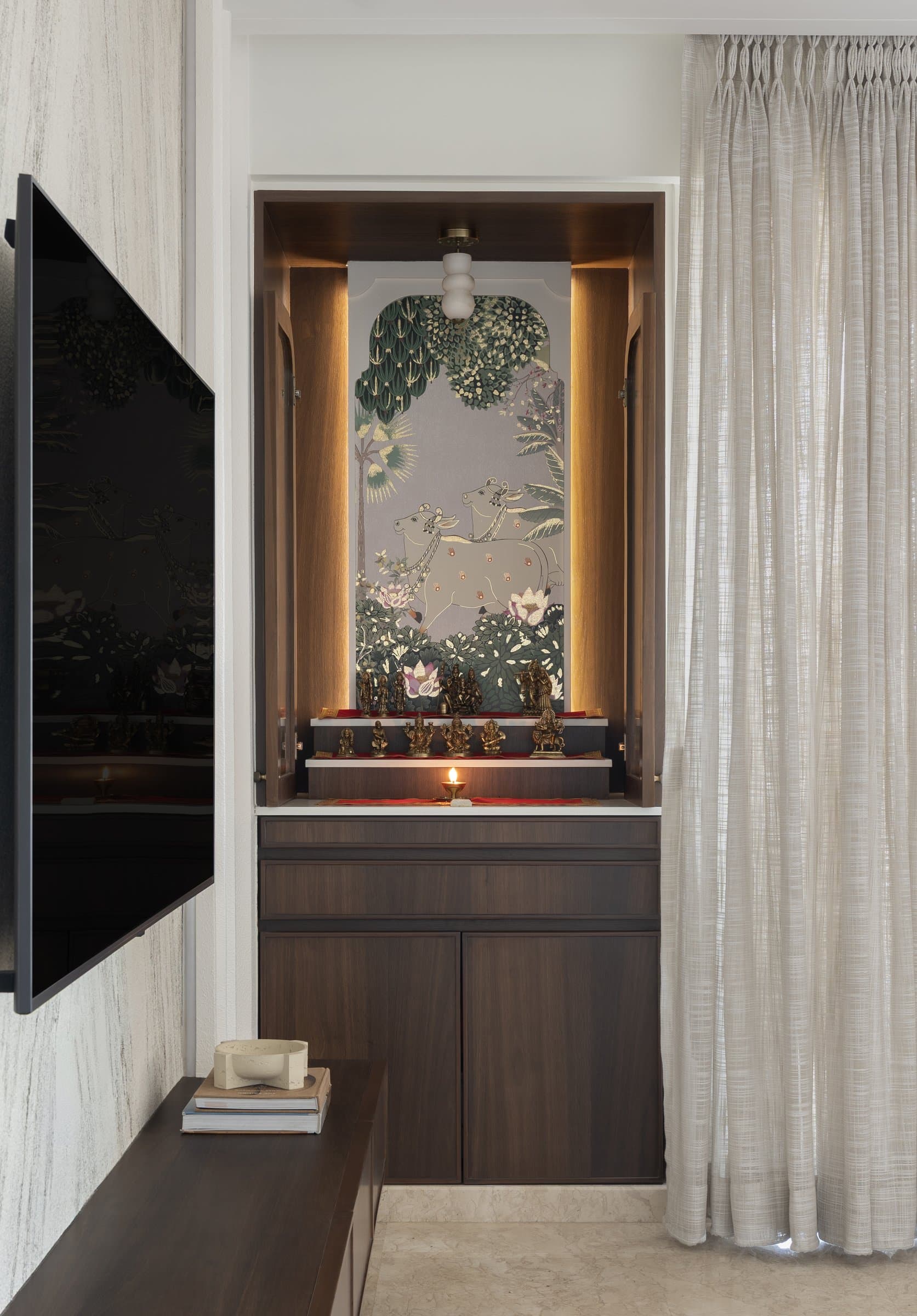 The puja alcove, where a pichwai-style artwork sits within a lit wooden niche