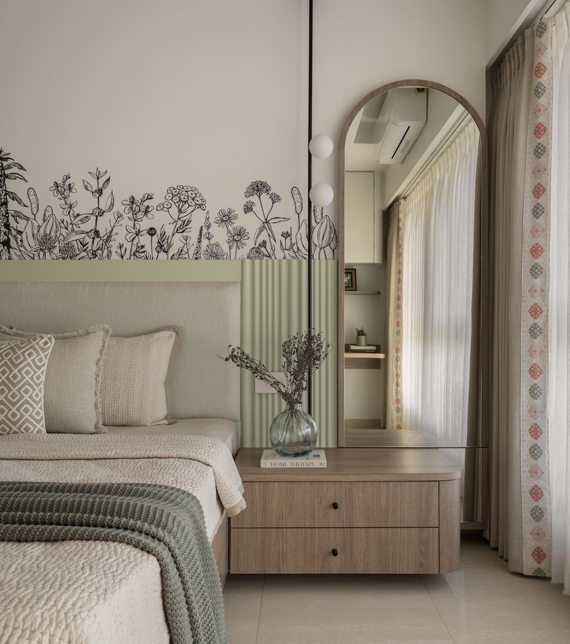 An arched floor mirror and wooden bedside chest, with a patterned curtain edge adding folk inflection