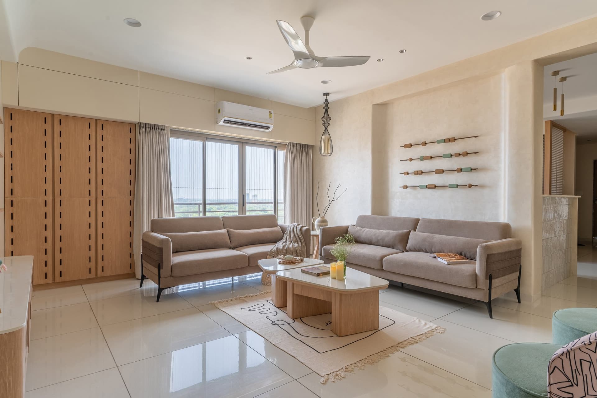 The living room, where two taupe sofas face each other across a composition held together by light and wooden joinery