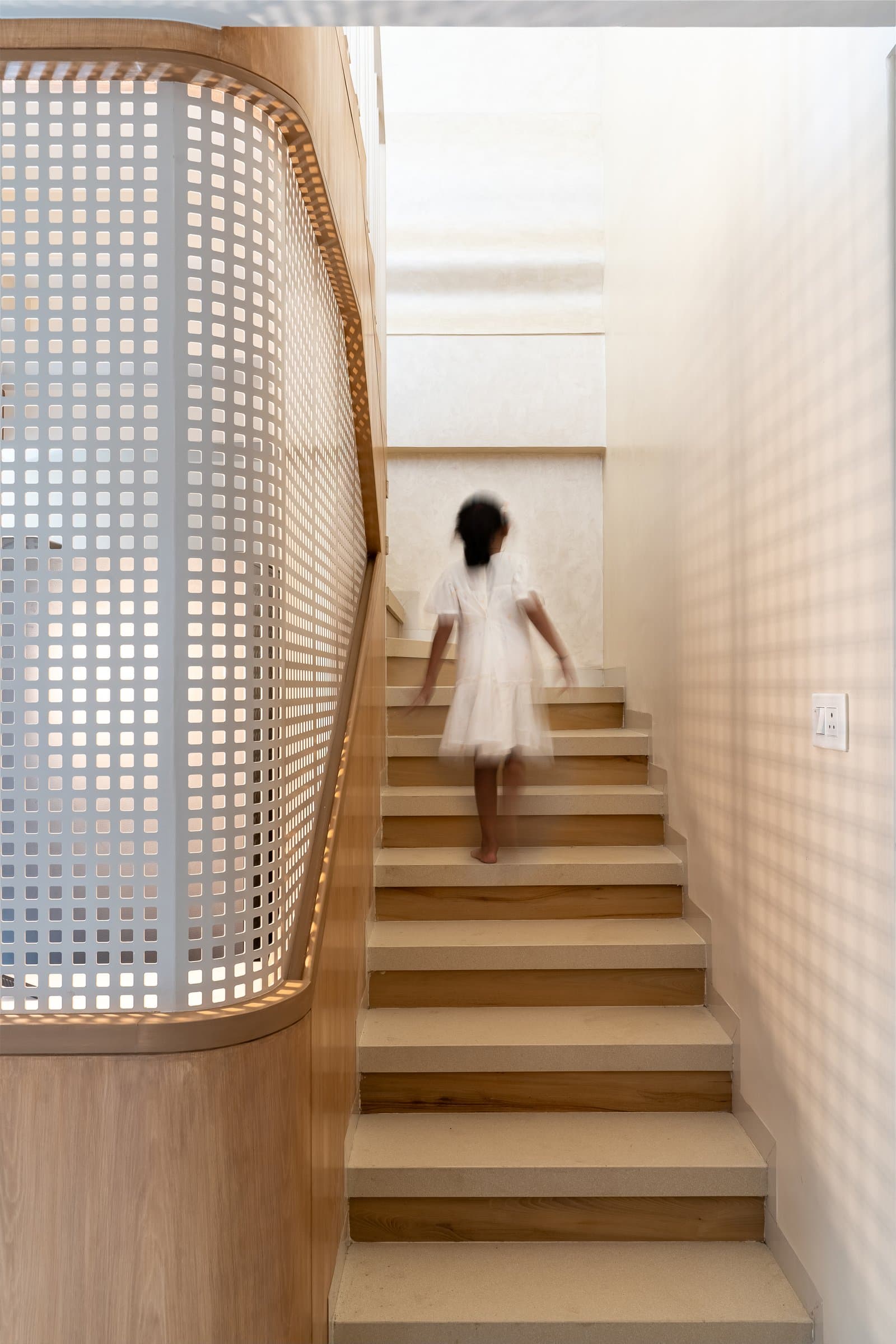 The staircase, where a curved wooden balustrade and perforated screen scatter patterned light across the ascent