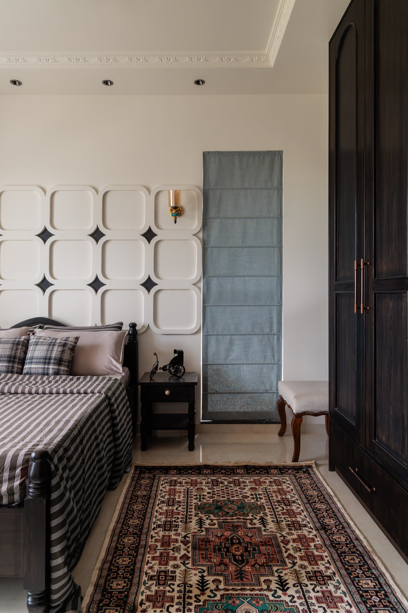 A side view of the guest room, pairing the sculpted panelling with a dark wardrobe and a muted blue roman shade