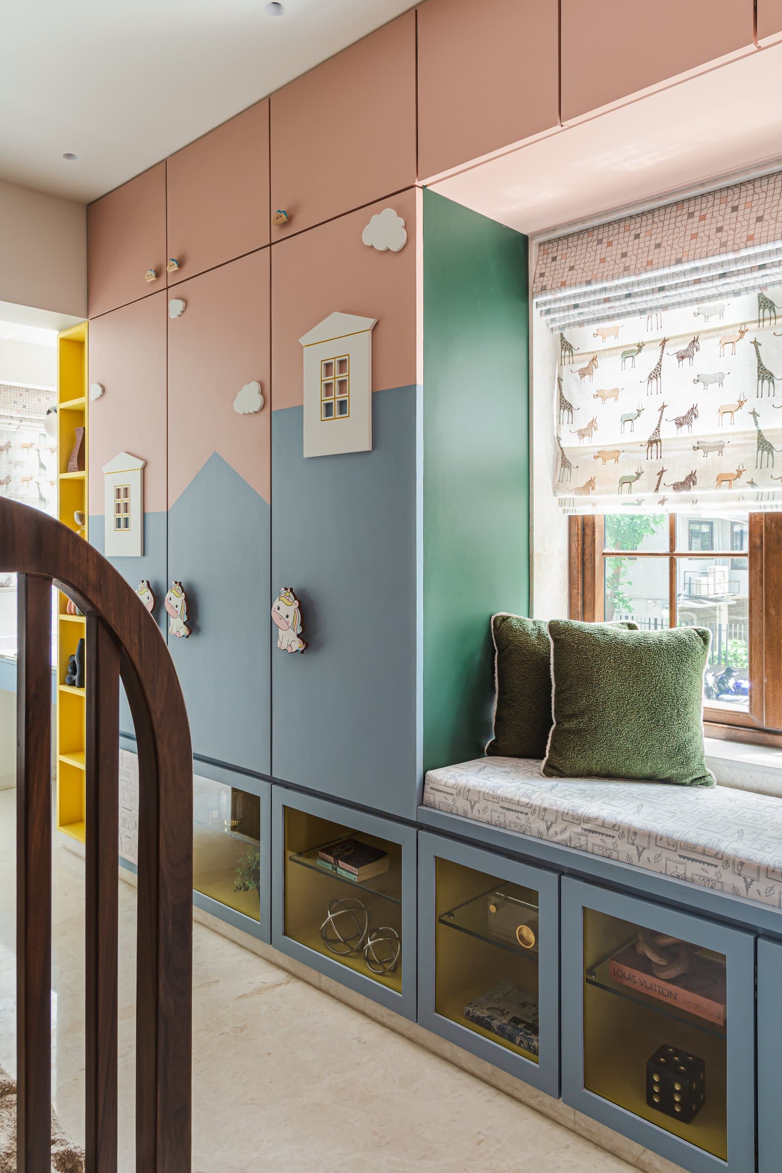 The second children's zone, where two-tone painted storage, a cushioned window seat and a yellow-lined shelving unit introduce the home's most playful shift in palette