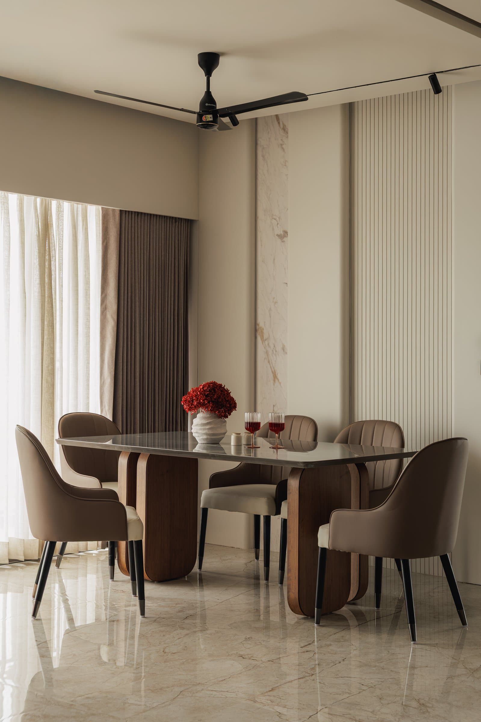 The dining area, with its rectangular table on sculptural wooden pedestals set against a ribbed cream and marble composition