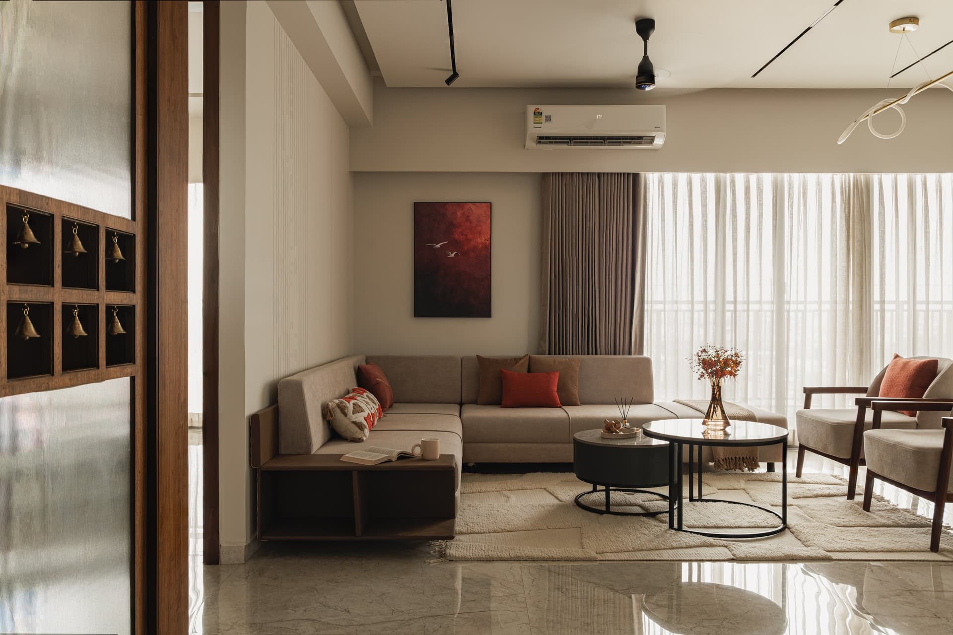 The living room, where a corner sofa in warm greige meets a single oxblood painting against a ribbed cream wall