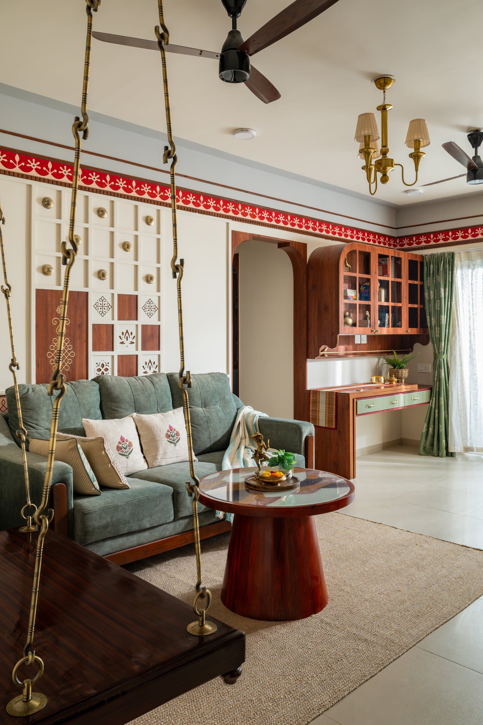 The living room, where a red-and-ivory painted border, a muted sage sofa and a suspended wooden swing establish the home's heritage-inspired language