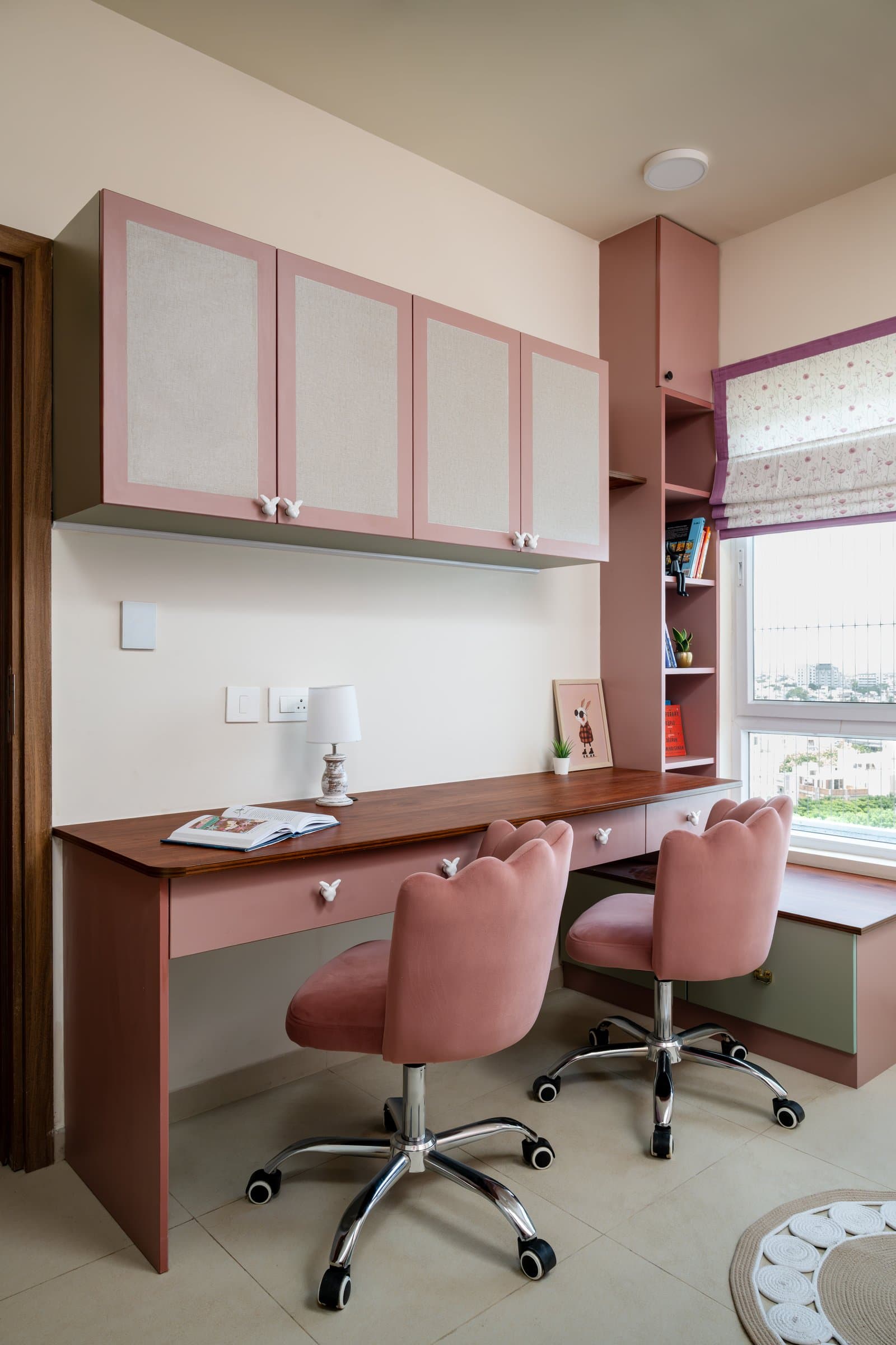 A study corner within the children's room, organised around a long wooden-topped desk with dusty-pink fronts and velvet task chairs