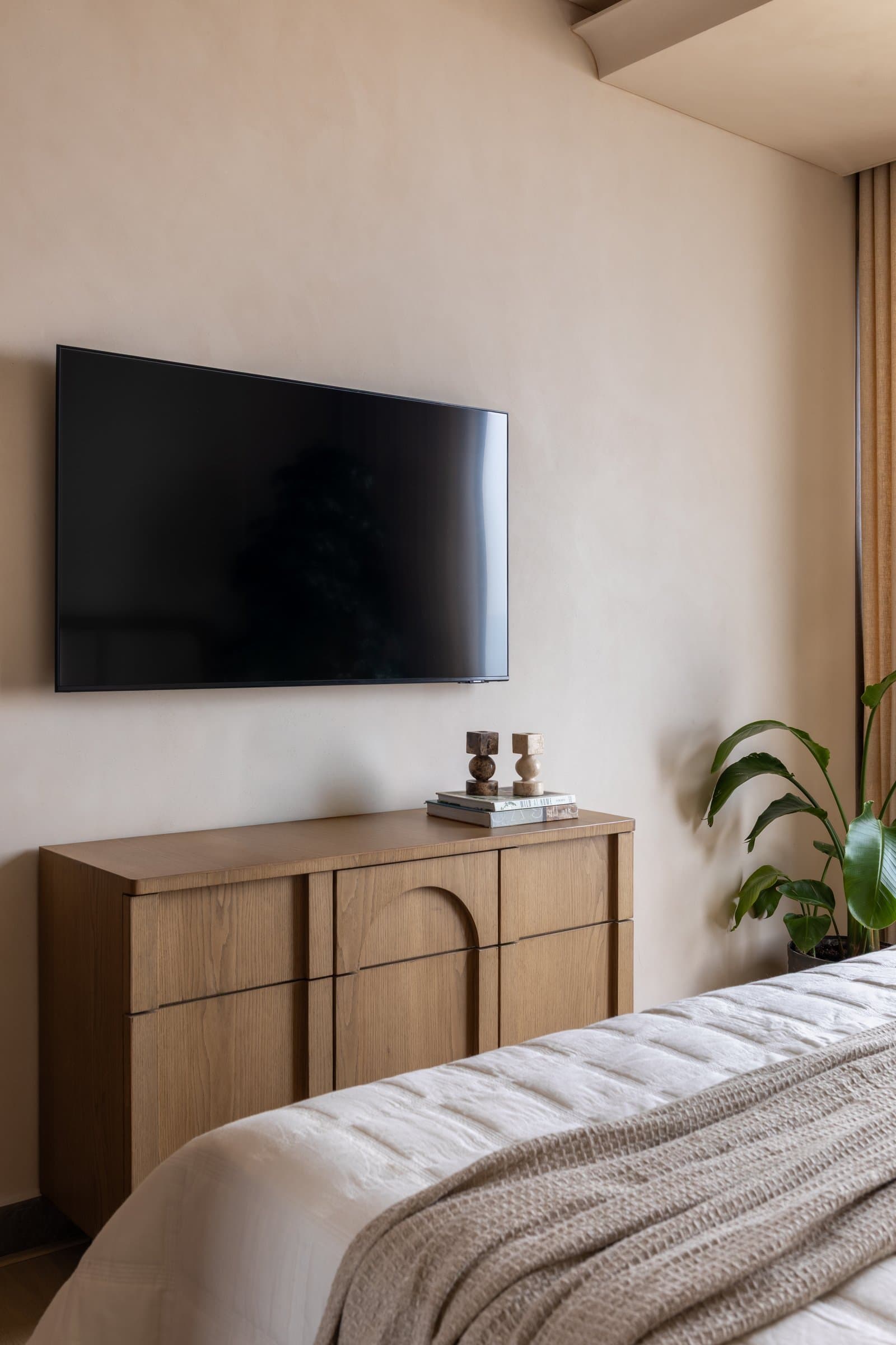 Opposite the bed, a veneered oak chest with an arched central detail carries the home's recurring softened geometry
