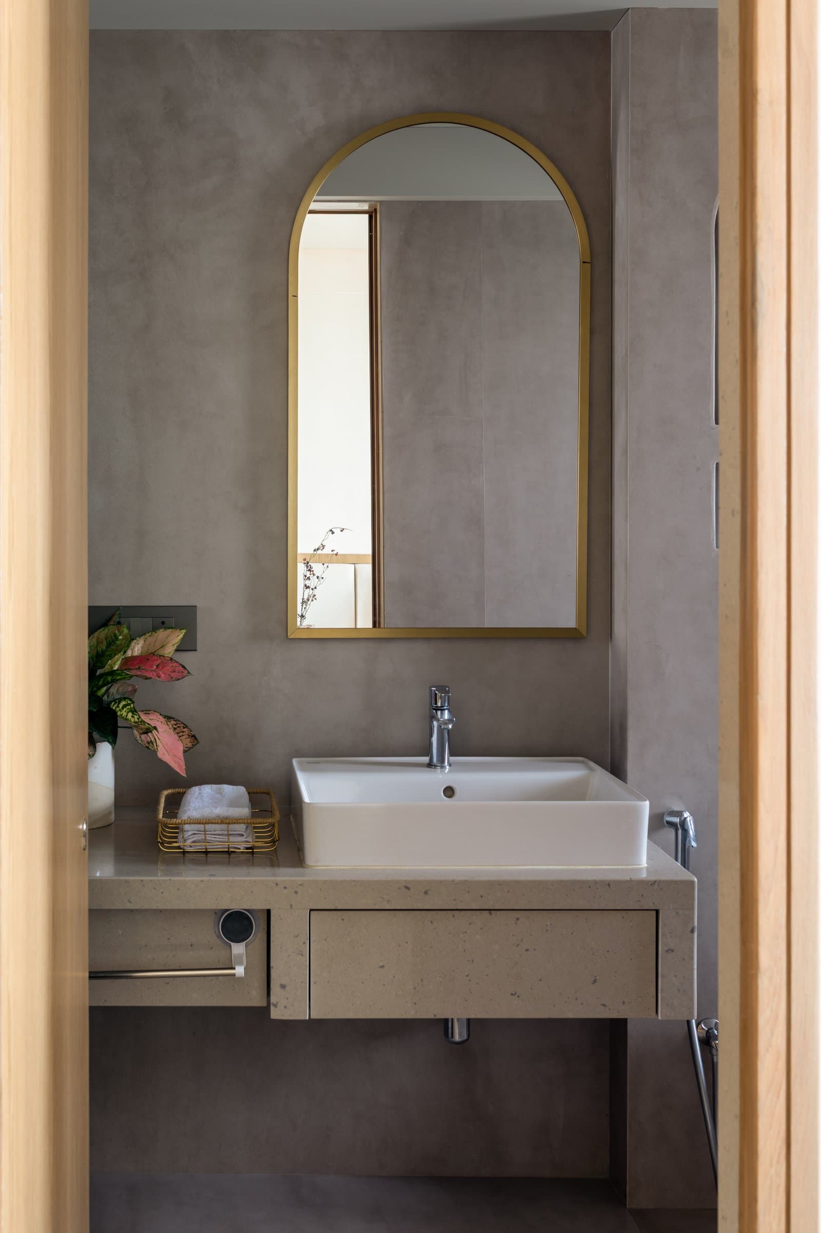 The second bathroom, where a floating speckled-stone vanity sits beneath a slim brass-framed arched mirror