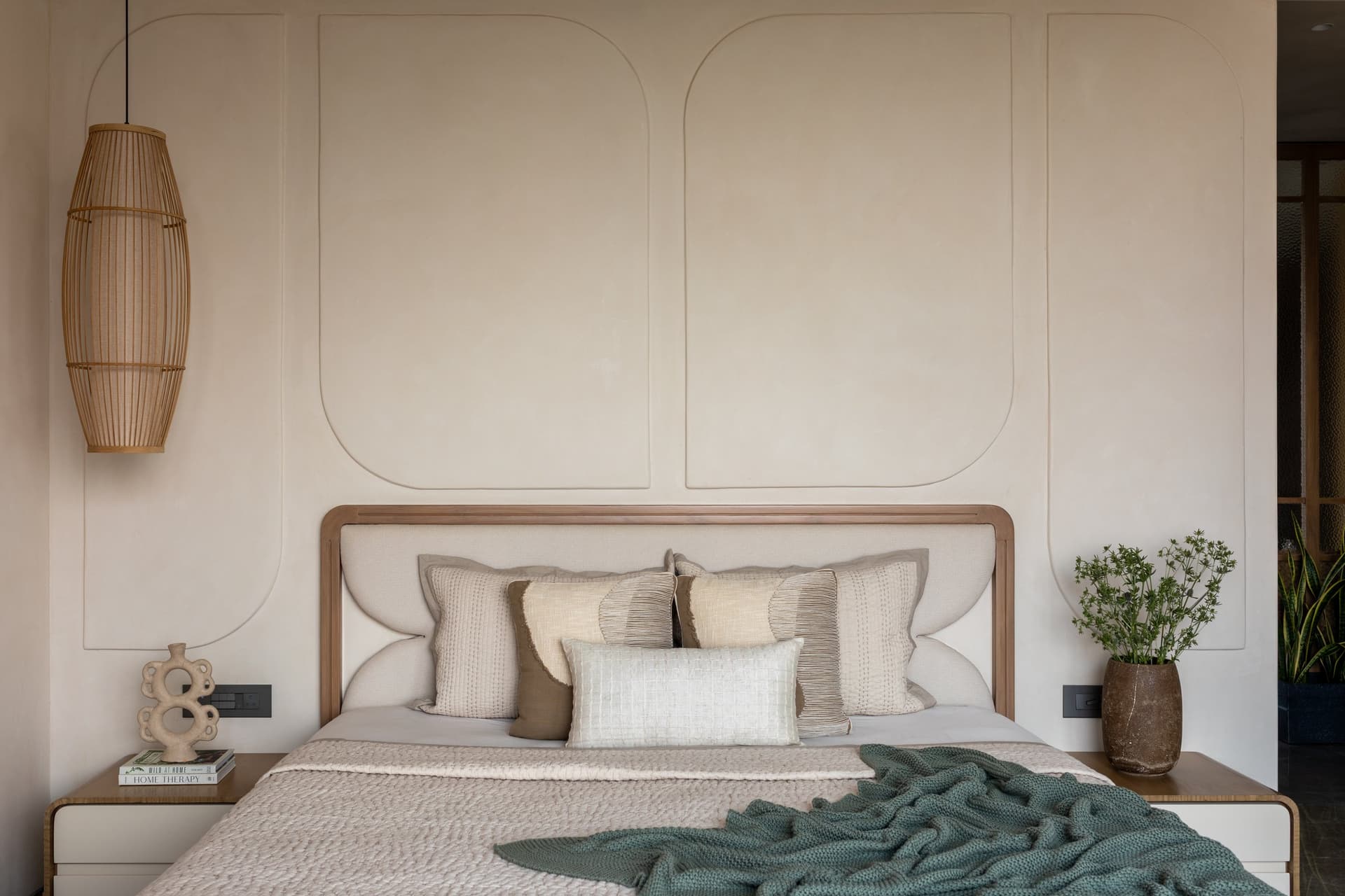 The primary bedroom, composed around a plastered feature wall whose curved recessed panels frame the headboard