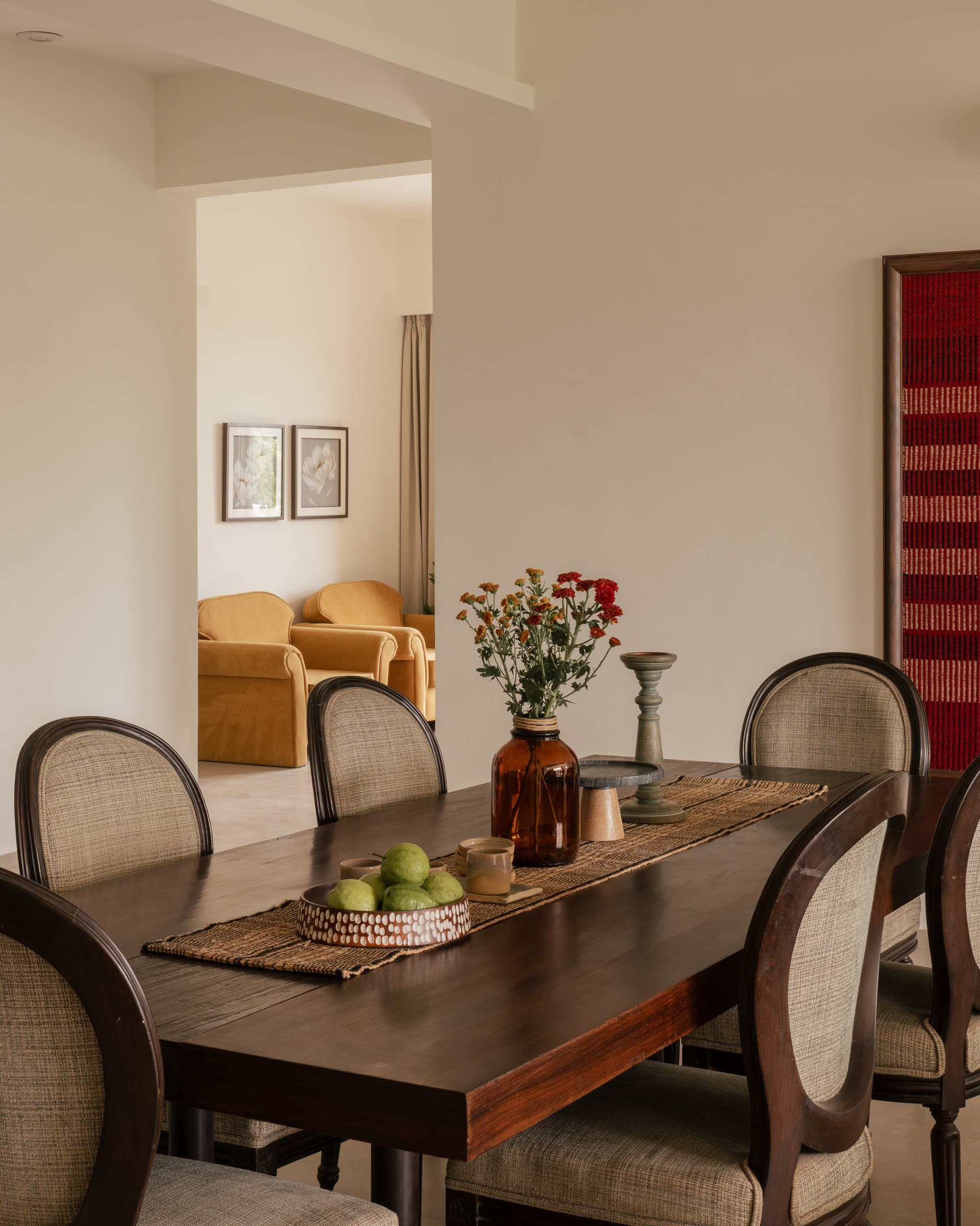 The dining area, with cane-backed chairs around a long dark wooden table and a glimpse through to the mustard armchairs beyond