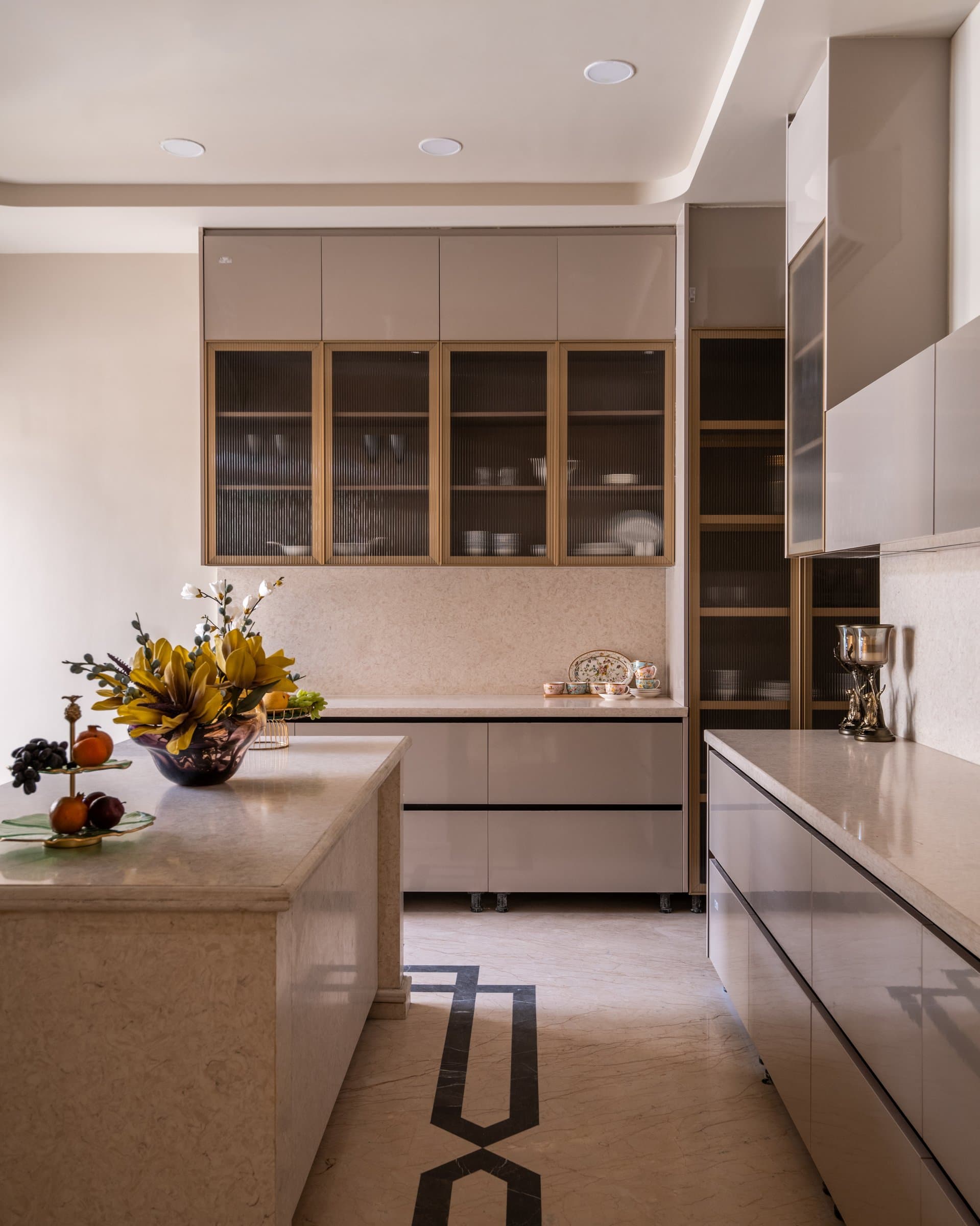 The kitchen, where glossy putty-toned cabinetry is softened by fluted glass-fronted display units banded in wood